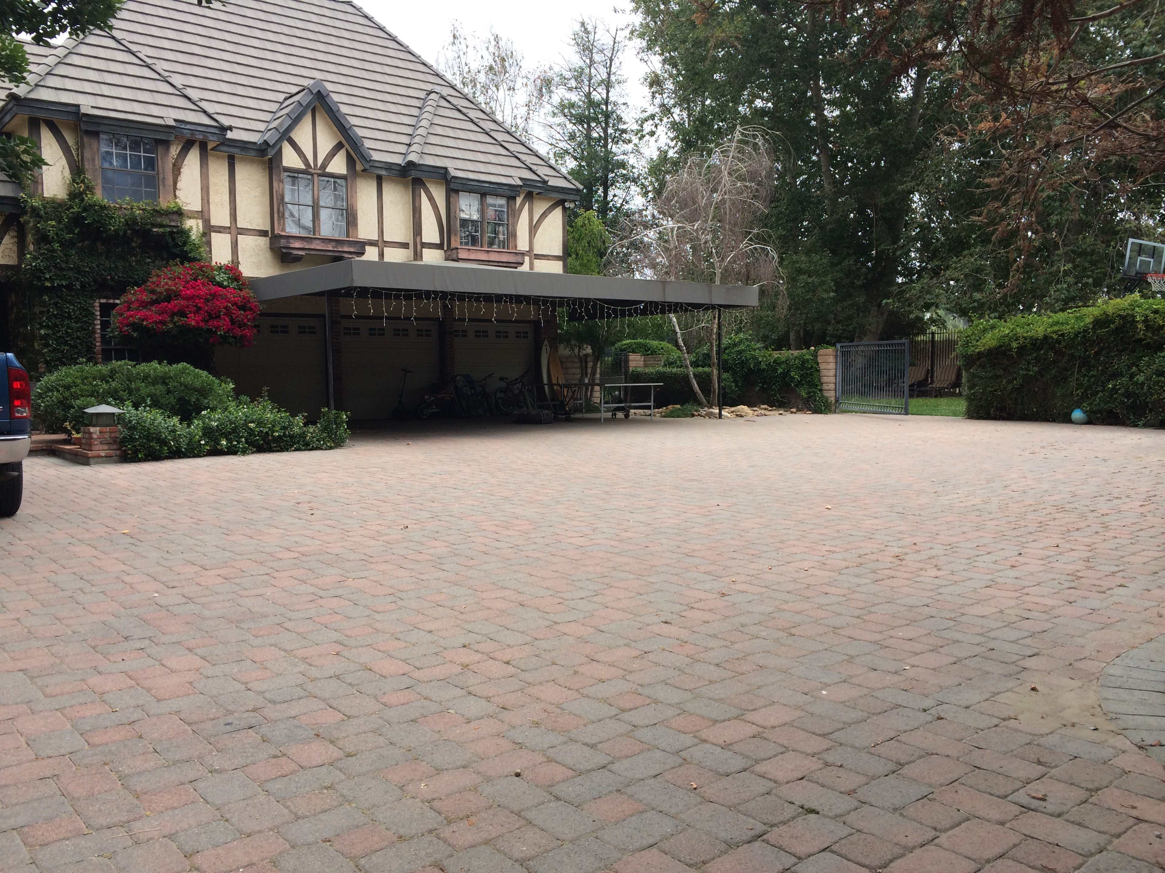 A large brick-paved driveway leads to a house with a covered entryway adorned with greenery and flowers.