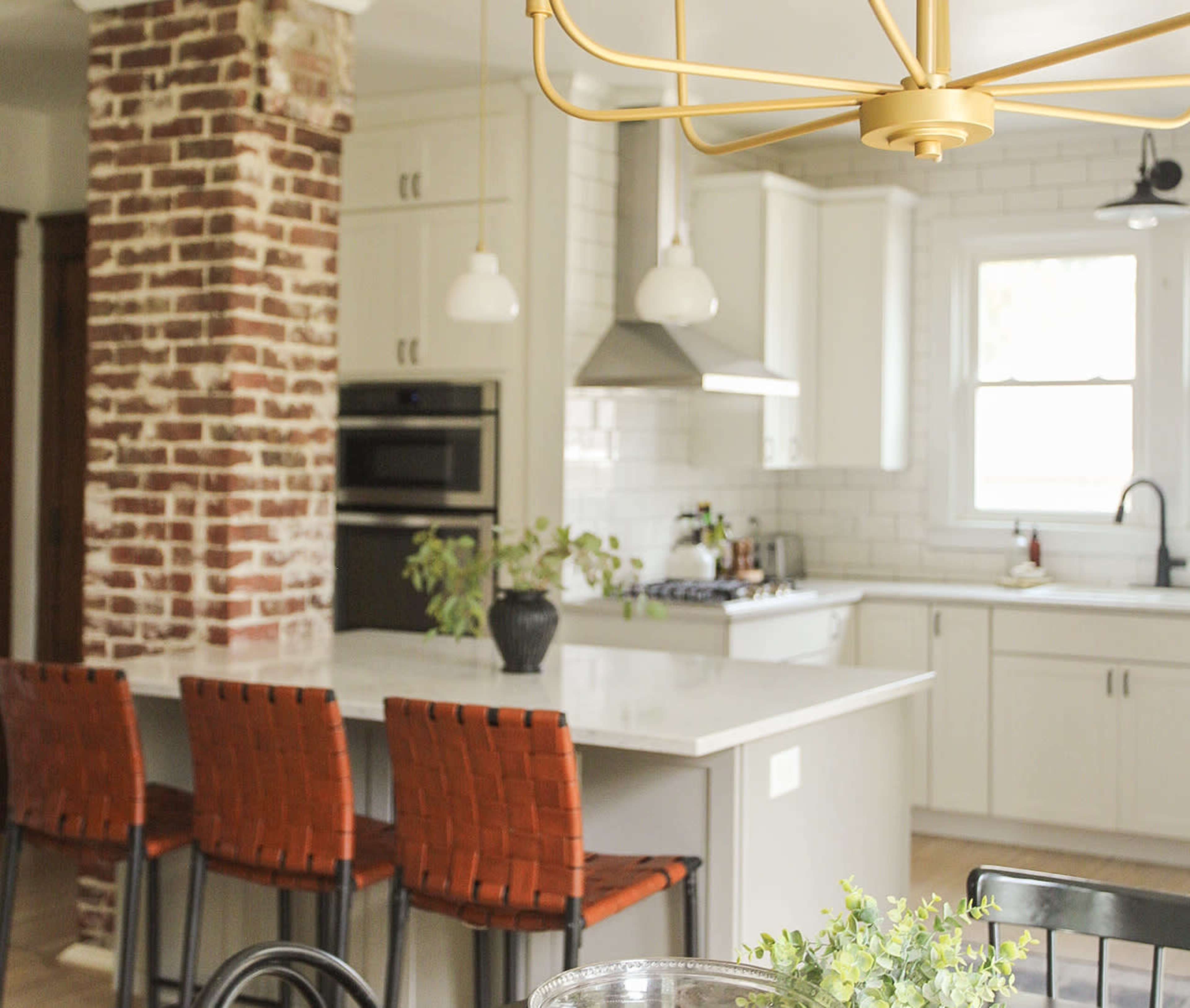 A modern kitchen with a brick accent wall, white cabinetry, and four brown woven bar stools at a kitchen island.