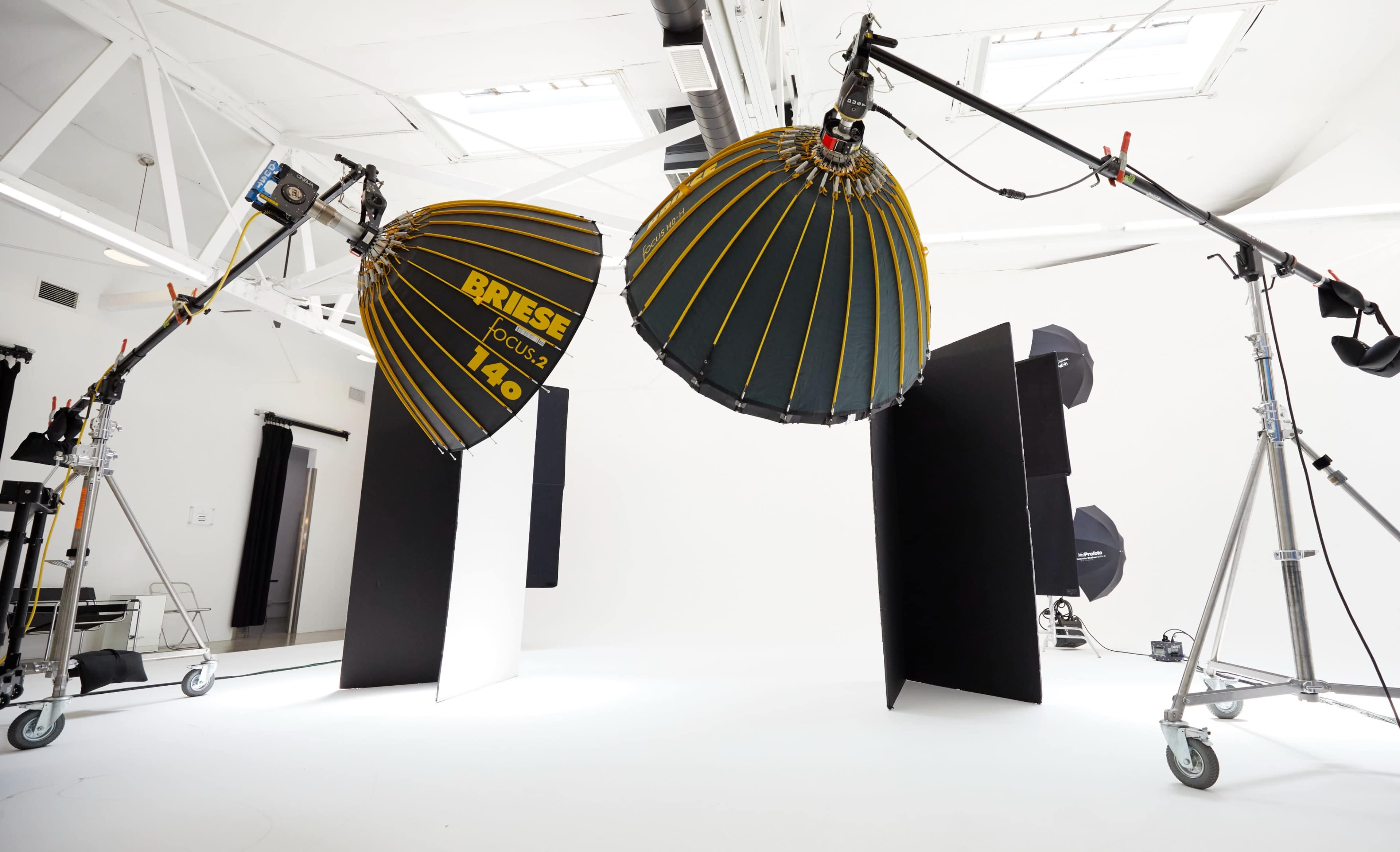 The image shows a photography studio setup with two large softboxes positioned on light stands, surrounded by black panels and various equipment on wheels.