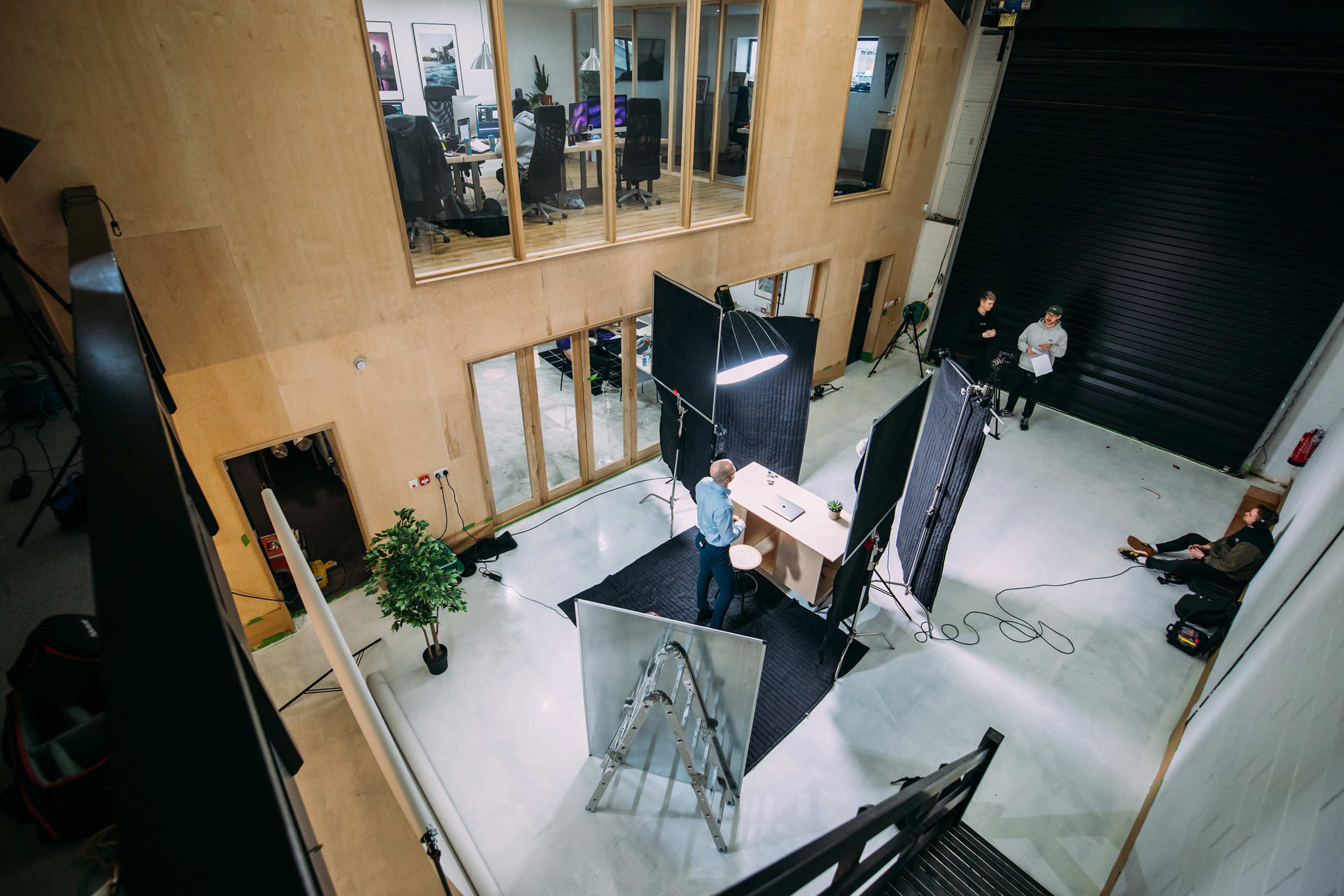 A person stands behind a table with lighting equipment and screens in a spacious, modern office setting.