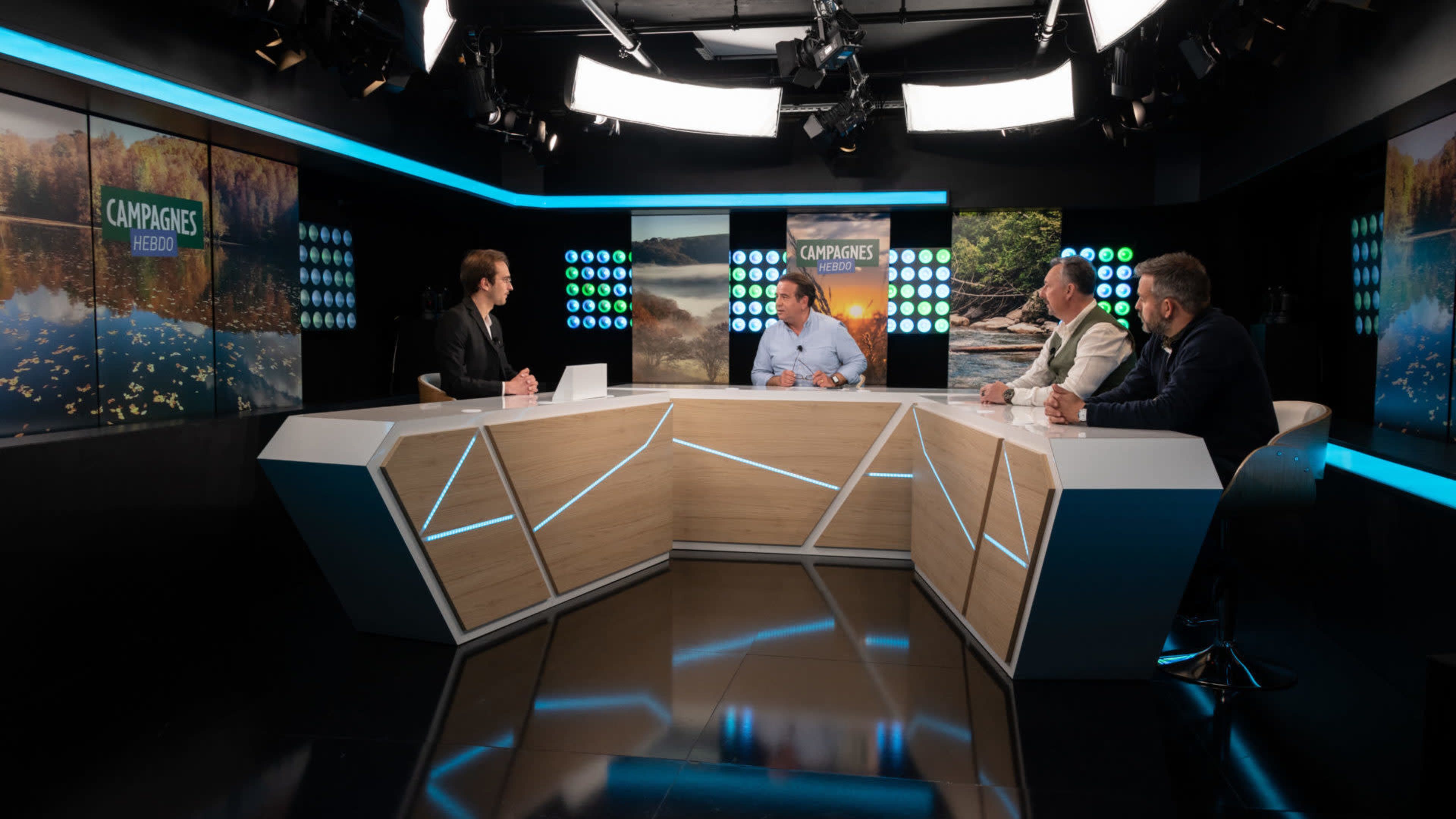 The image shows a television studio set with four people seated at a modern table, discussing topics related to a nature-themed broadcast.