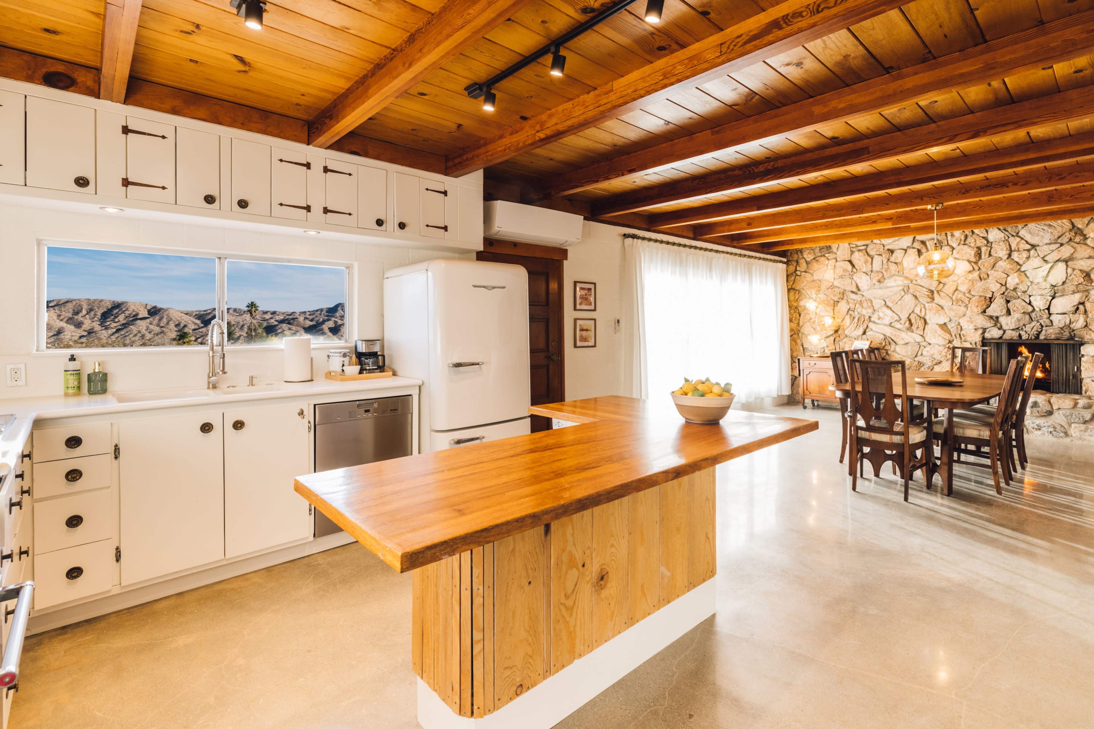 A spacious kitchen features a wooden island, white cabinetry, and an adjoining dining area with a stone fireplace.