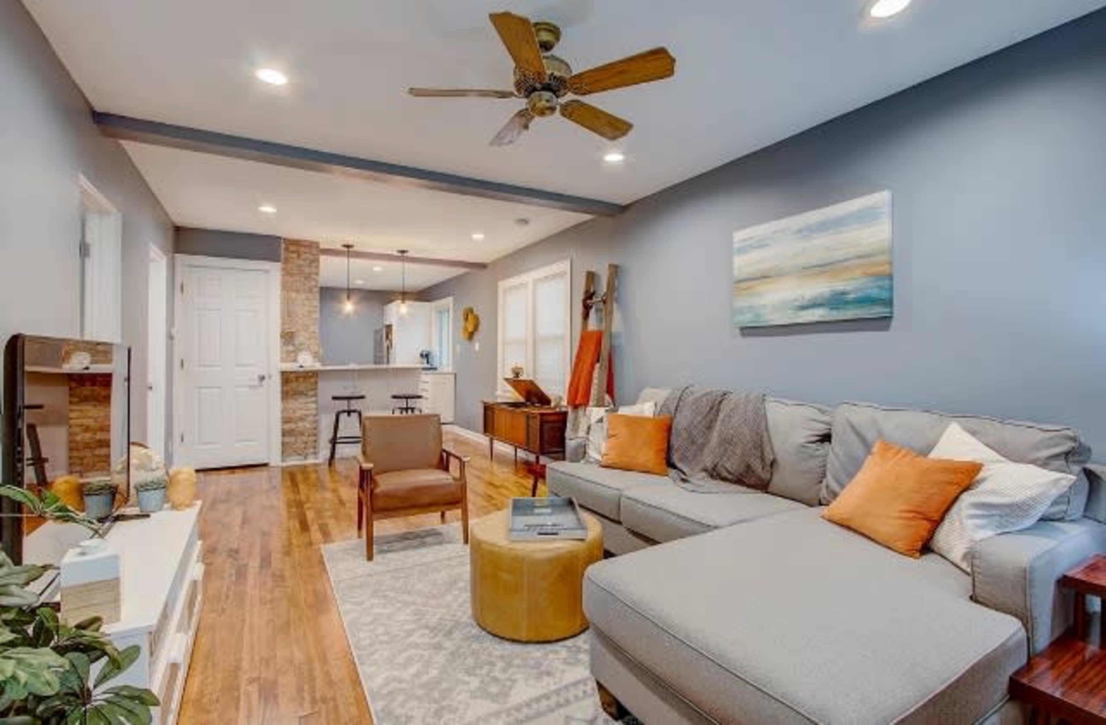 A living room with a sectional sofa, a coffee table, and an open view of a kitchen area featuring a bar counter.