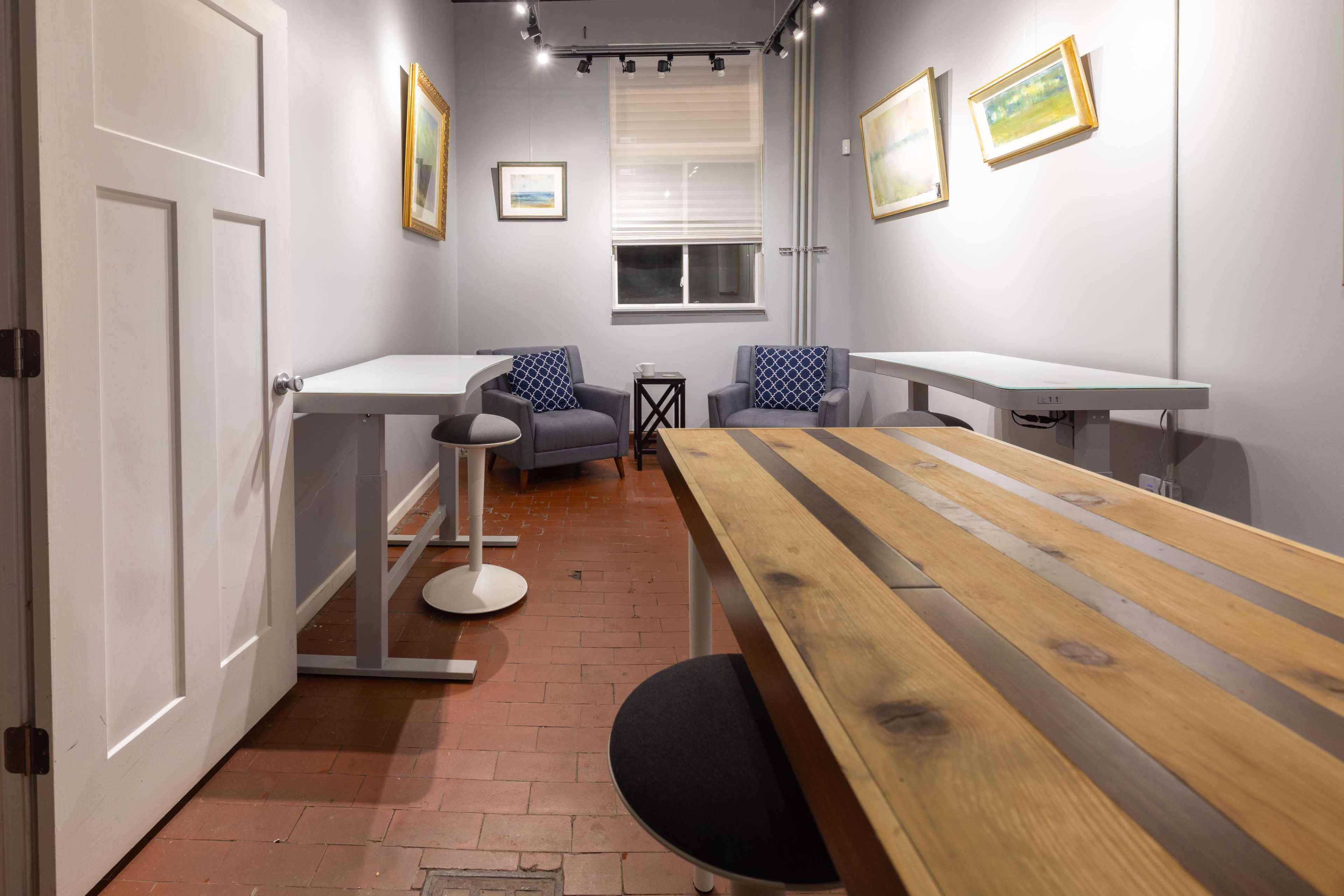A small, well-lit room with two work tables, a chair, and framed artwork on the walls.