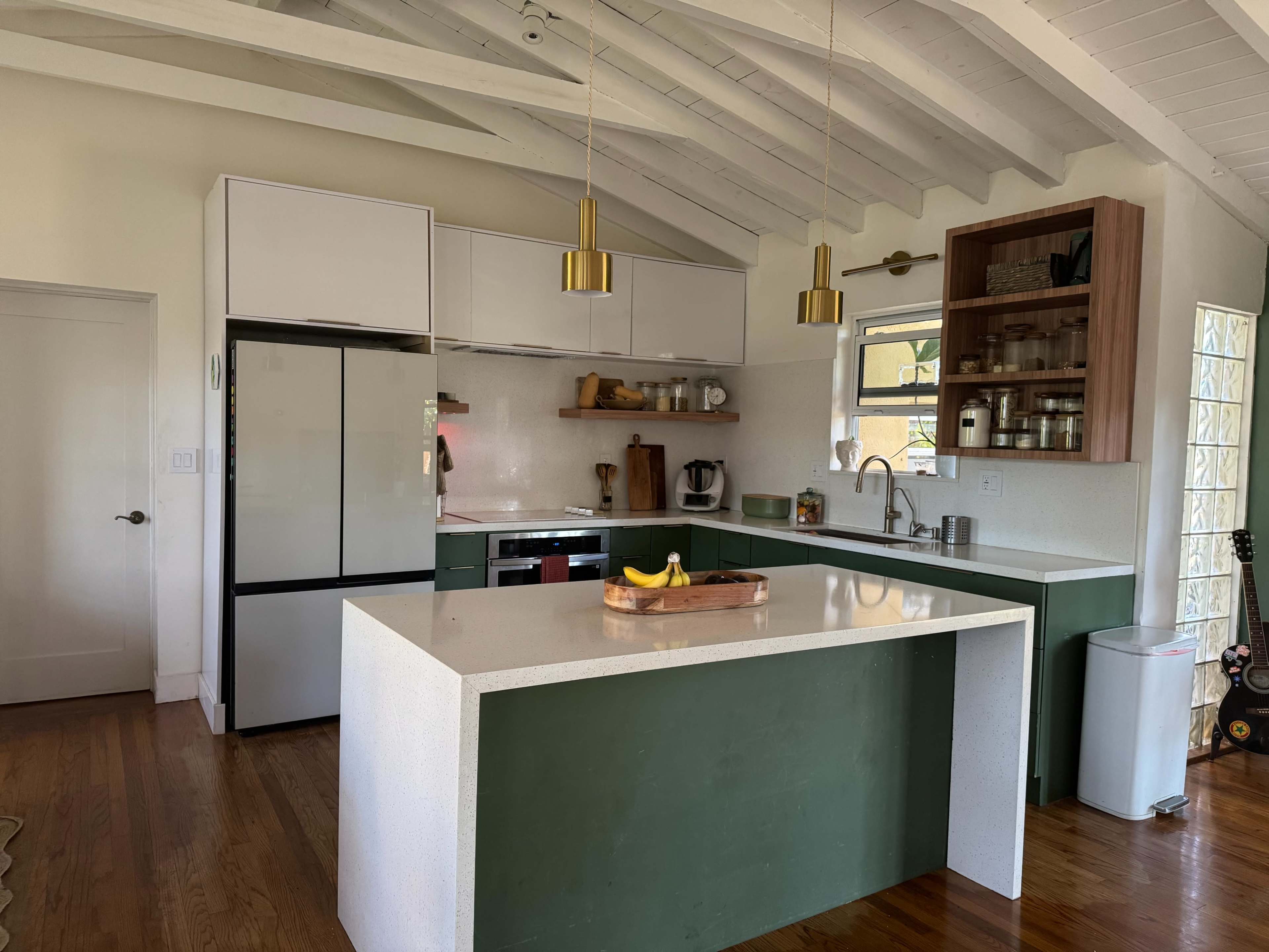 The image shows a modern kitchen featuring a green and white color scheme, with an island countertop, stainless steel appliances, and wooden accents.