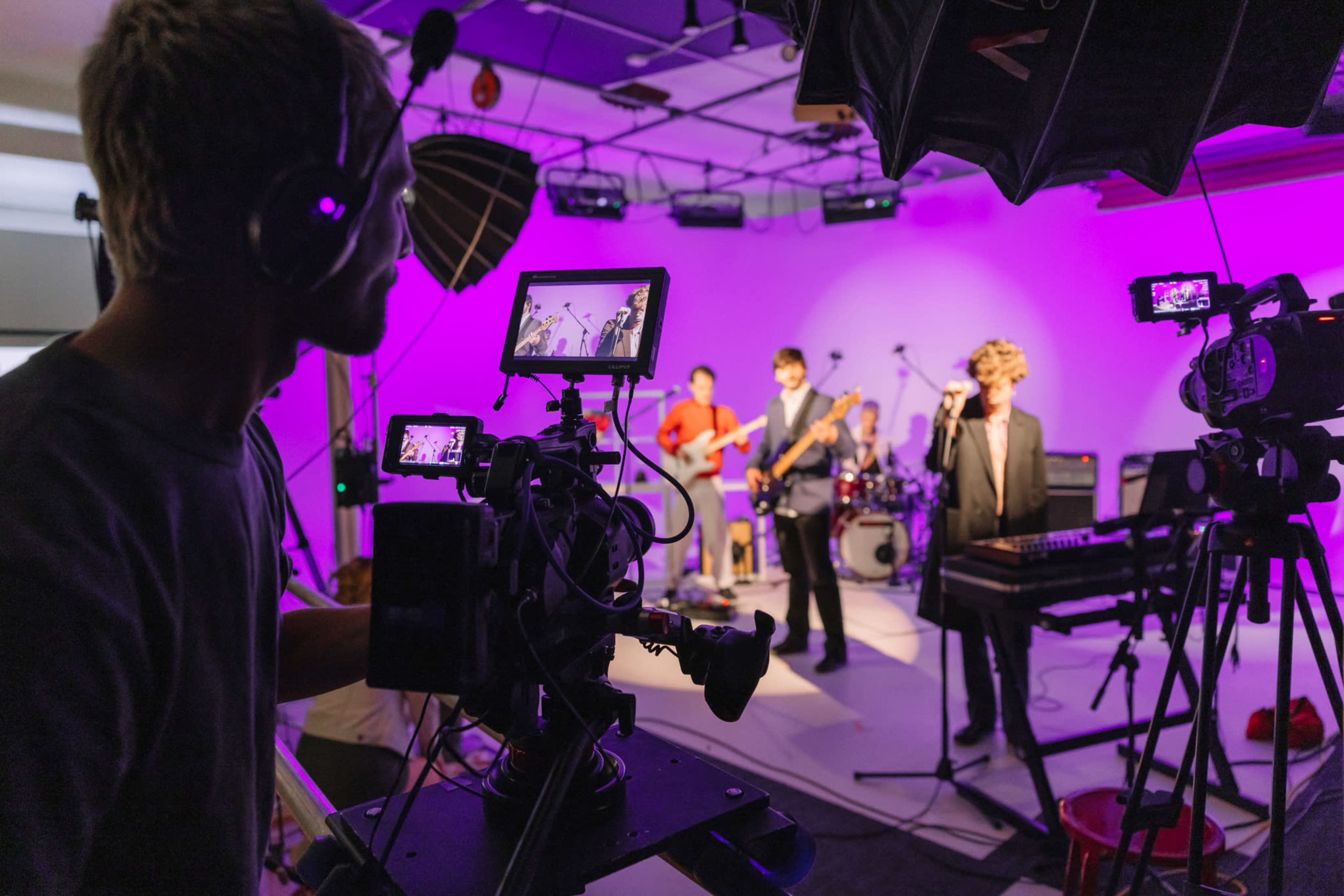 A band performs on stage while a camera operator records the performance on a video camera.