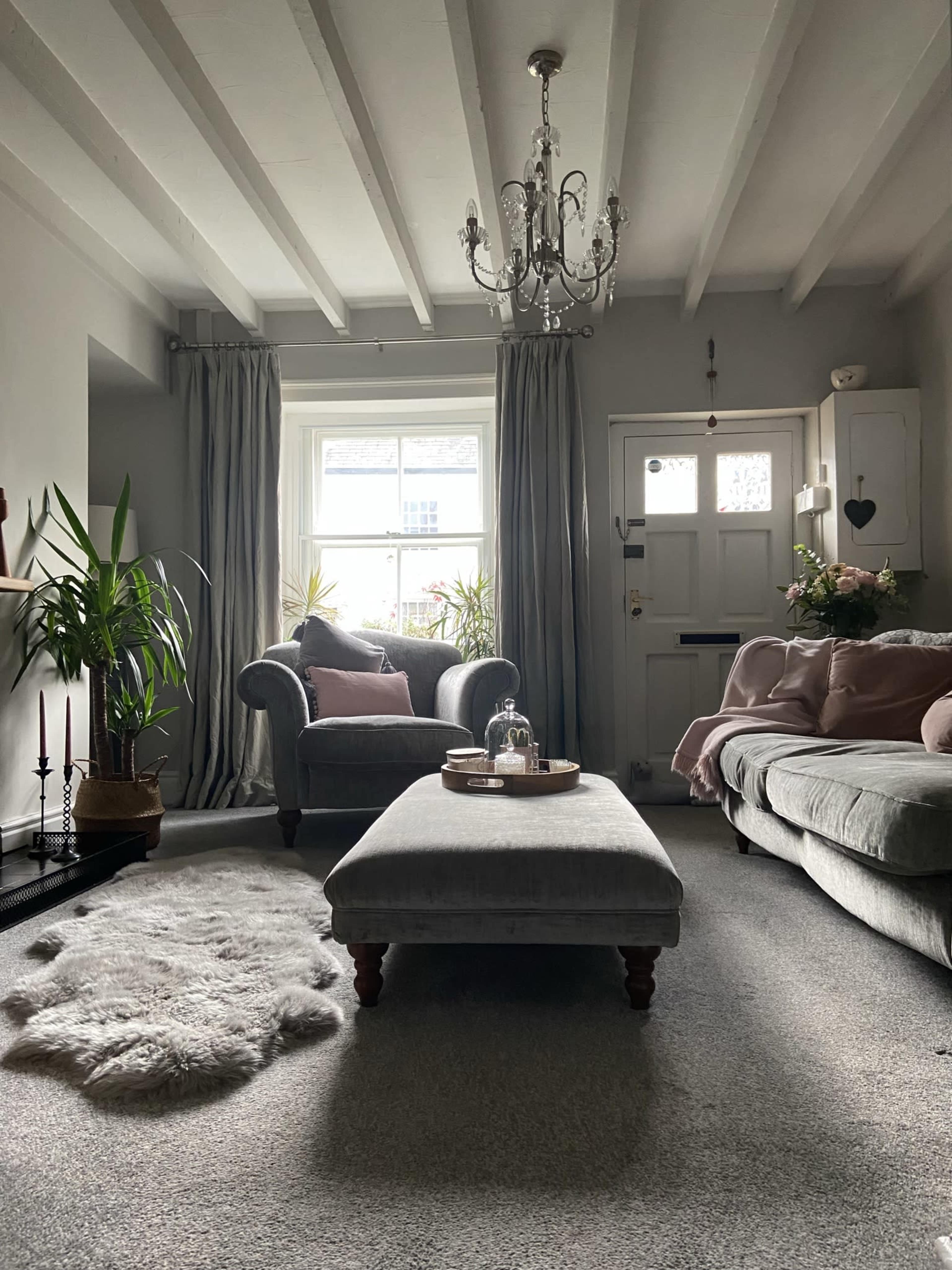 The living room features a gray color palette with a chandelier, a pair of sofas, a coffee table, and plants near a window.
