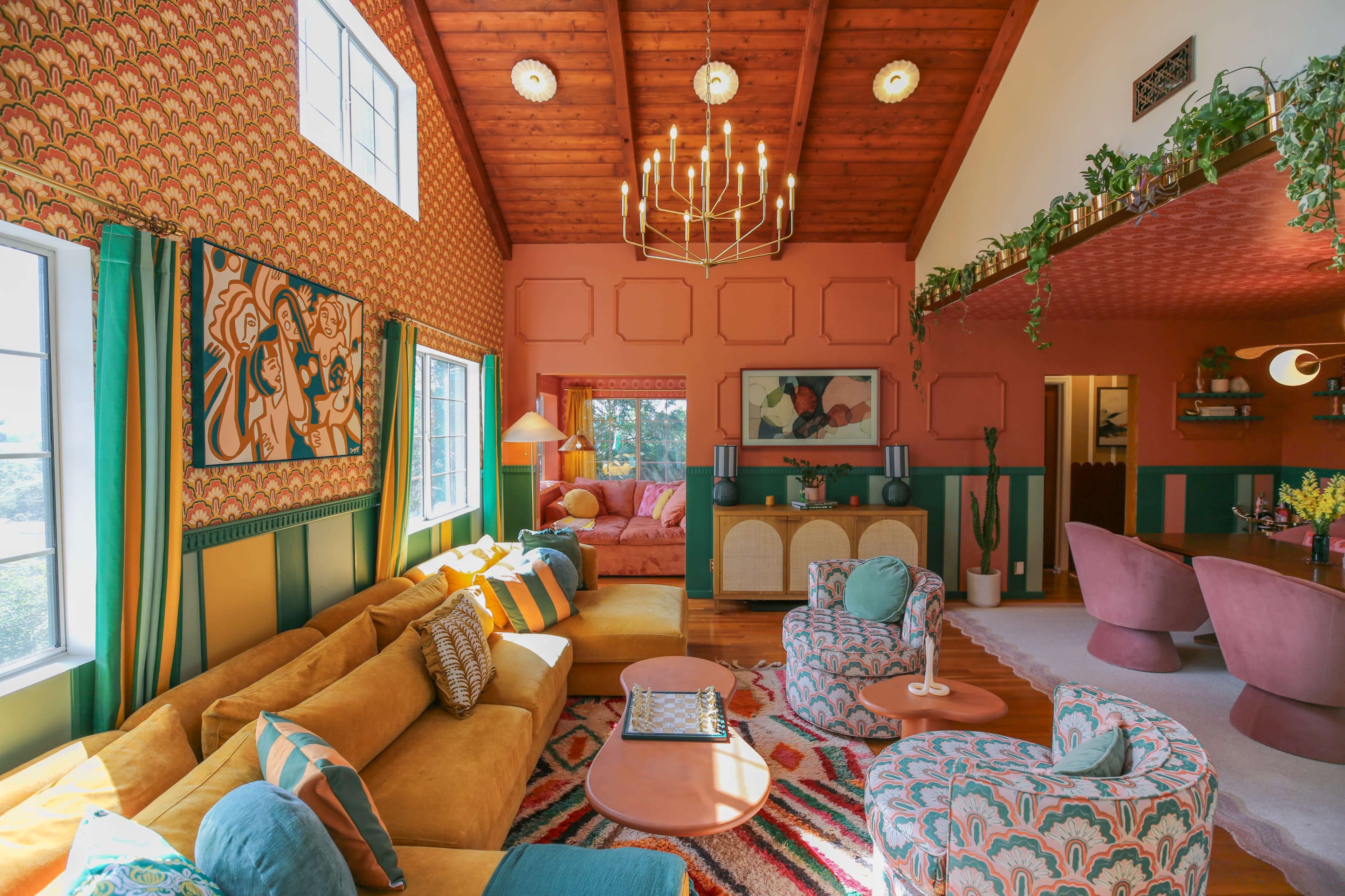 A vibrant living room featuring a mix of colorful furnishings, a tall wooden ceiling, and wall decorations with bold patterns.