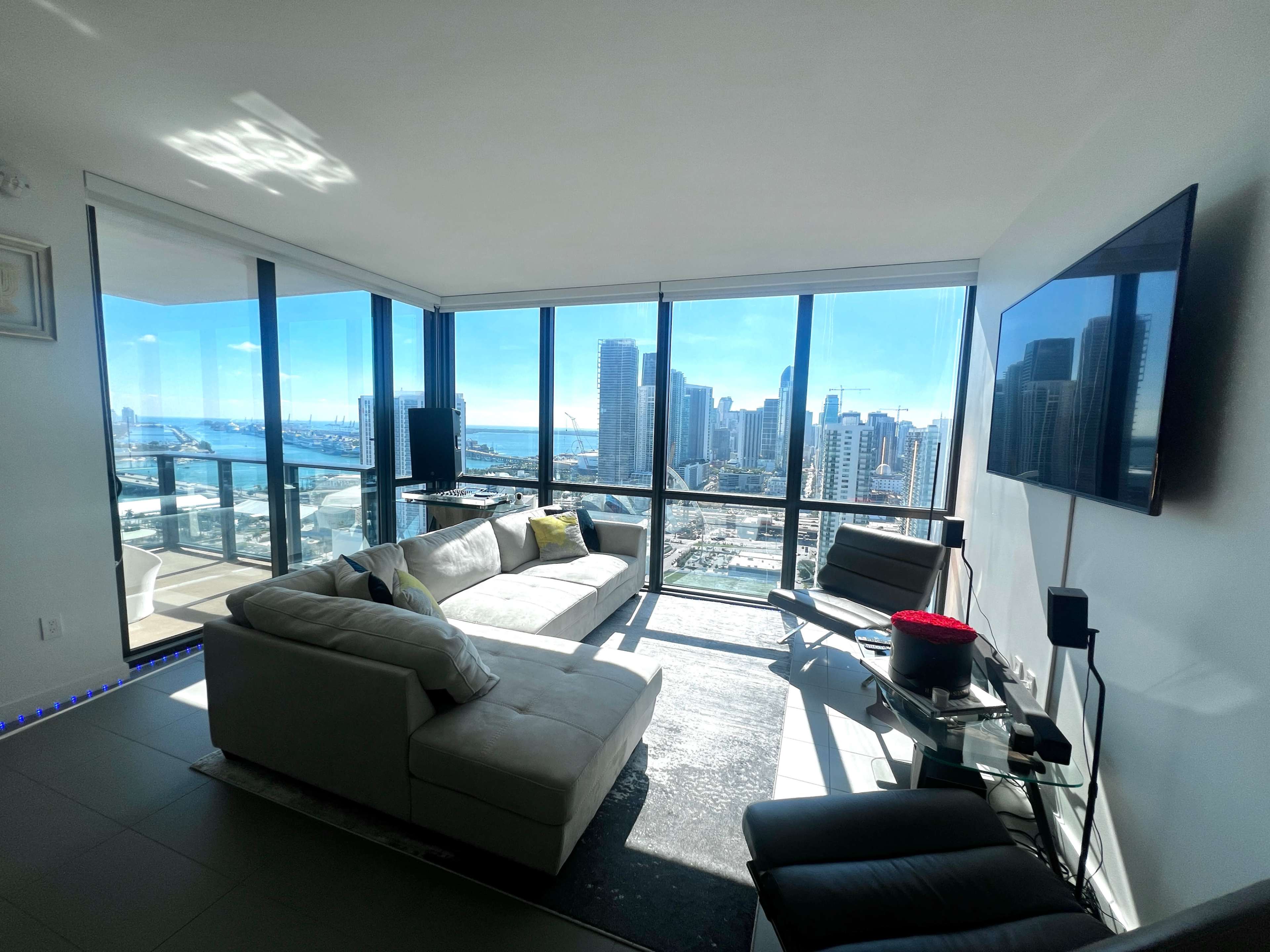 A modern living room features large windows with a panoramic view of a city skyline and waterfront.