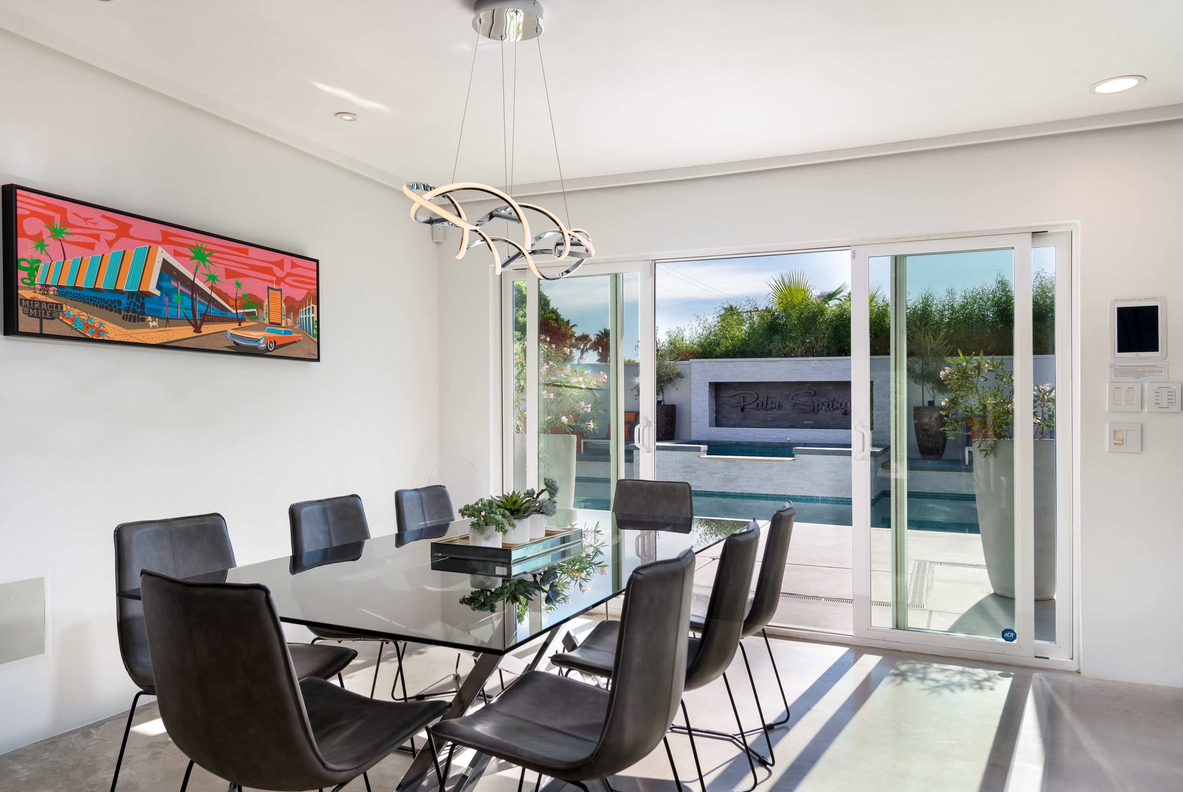 A modern dining room features a glass table surrounded by black chairs, with large sliding doors leading to a pool area.