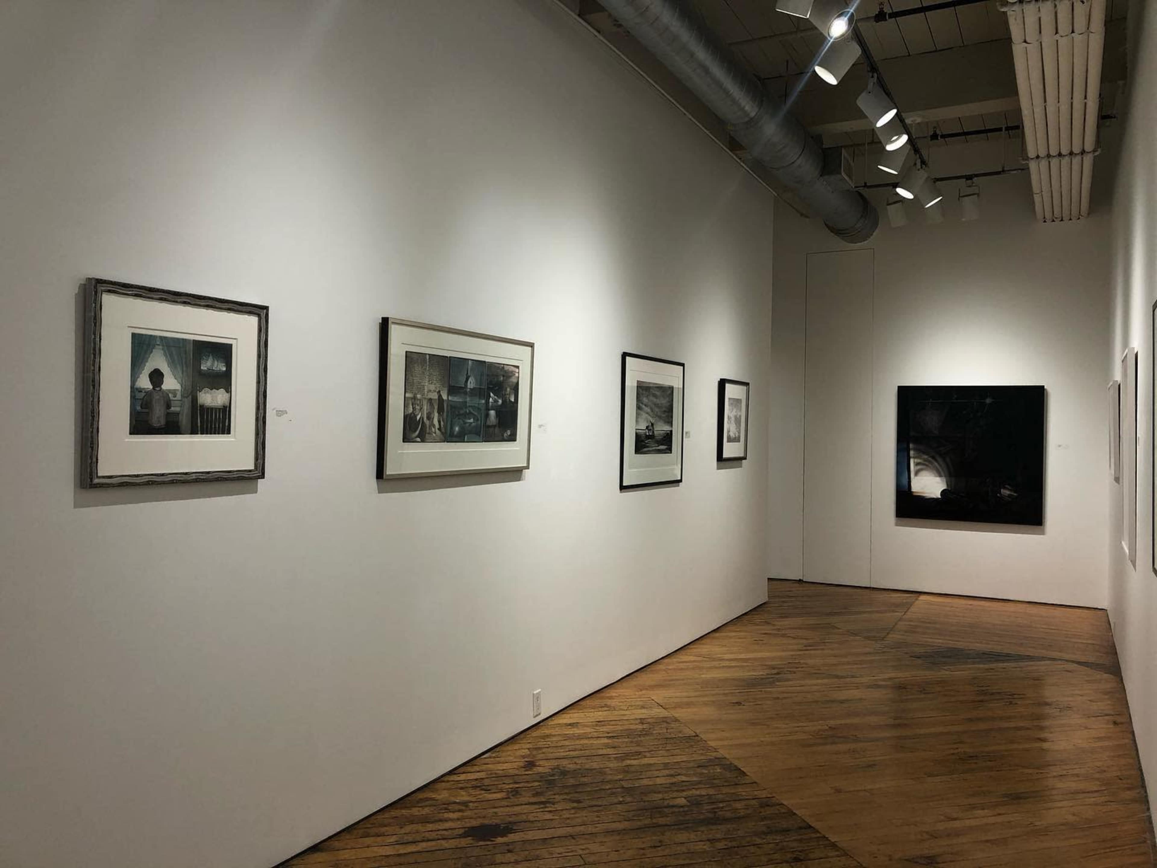 An art gallery with framed photographs displayed on white walls and wooden flooring.