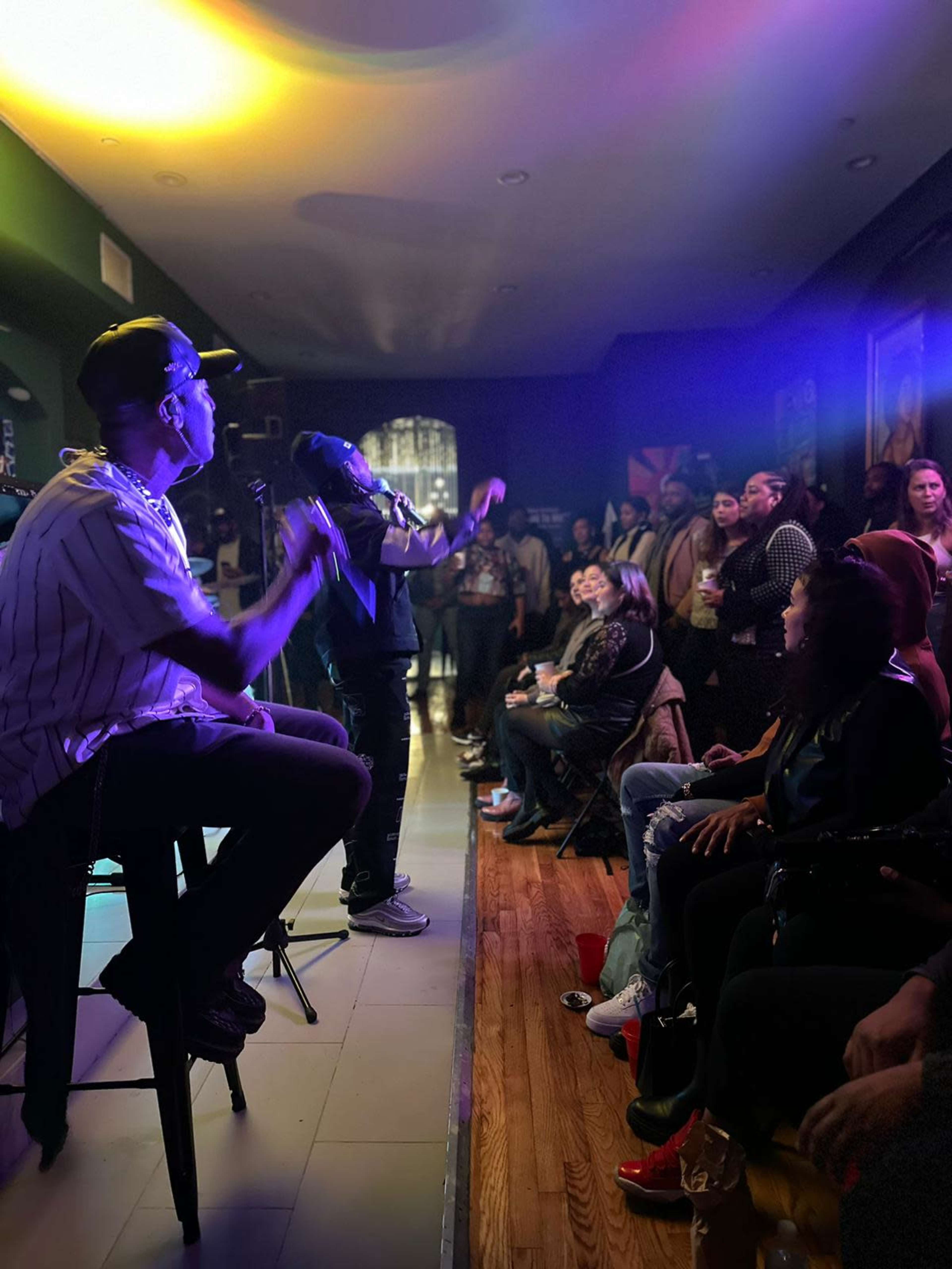 A performer sings on stage while an audience enjoys the show in a dimly lit venue.