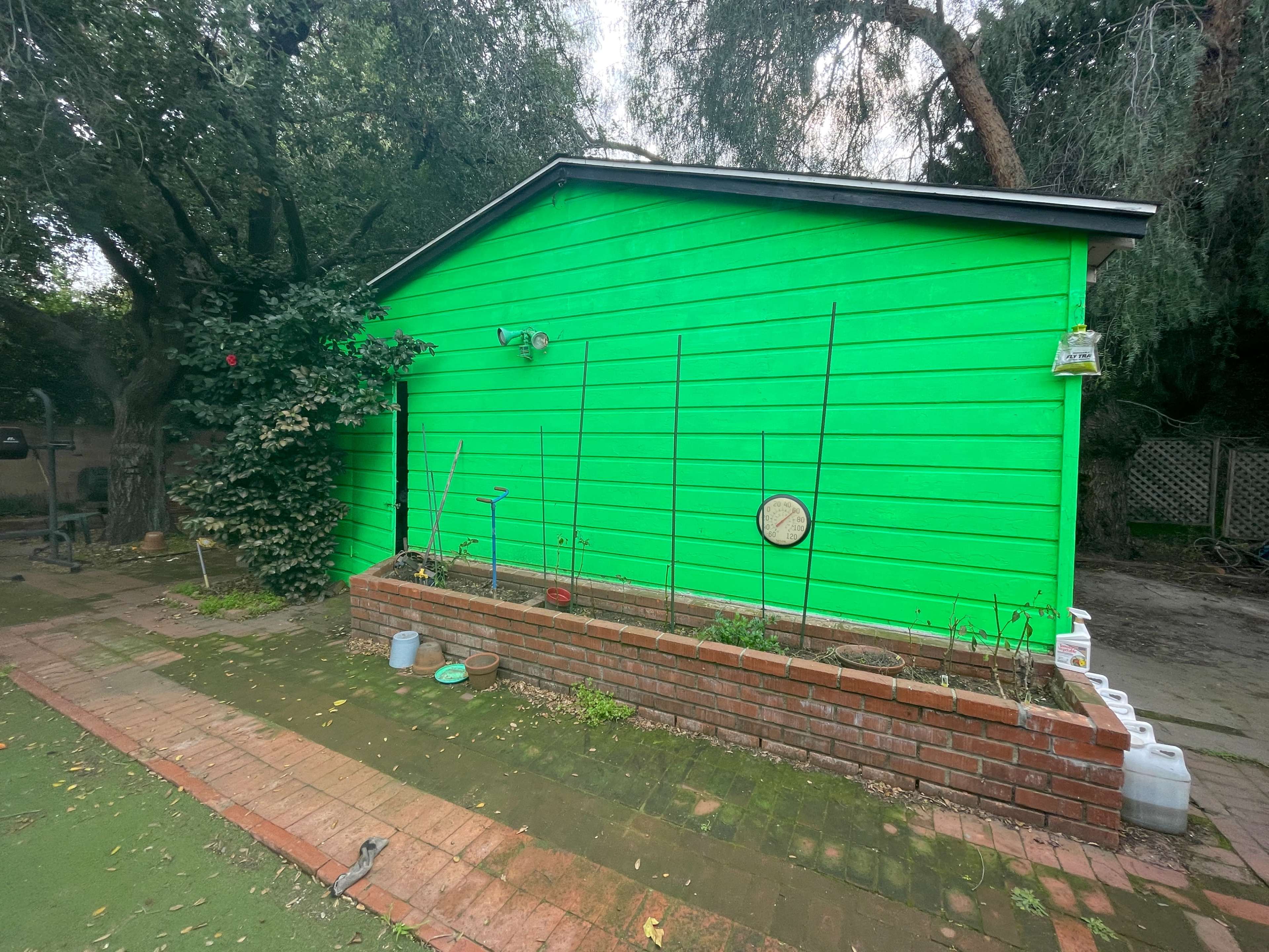 A bright green shed is surrounded by a brick planter and trees in a backyard setting.