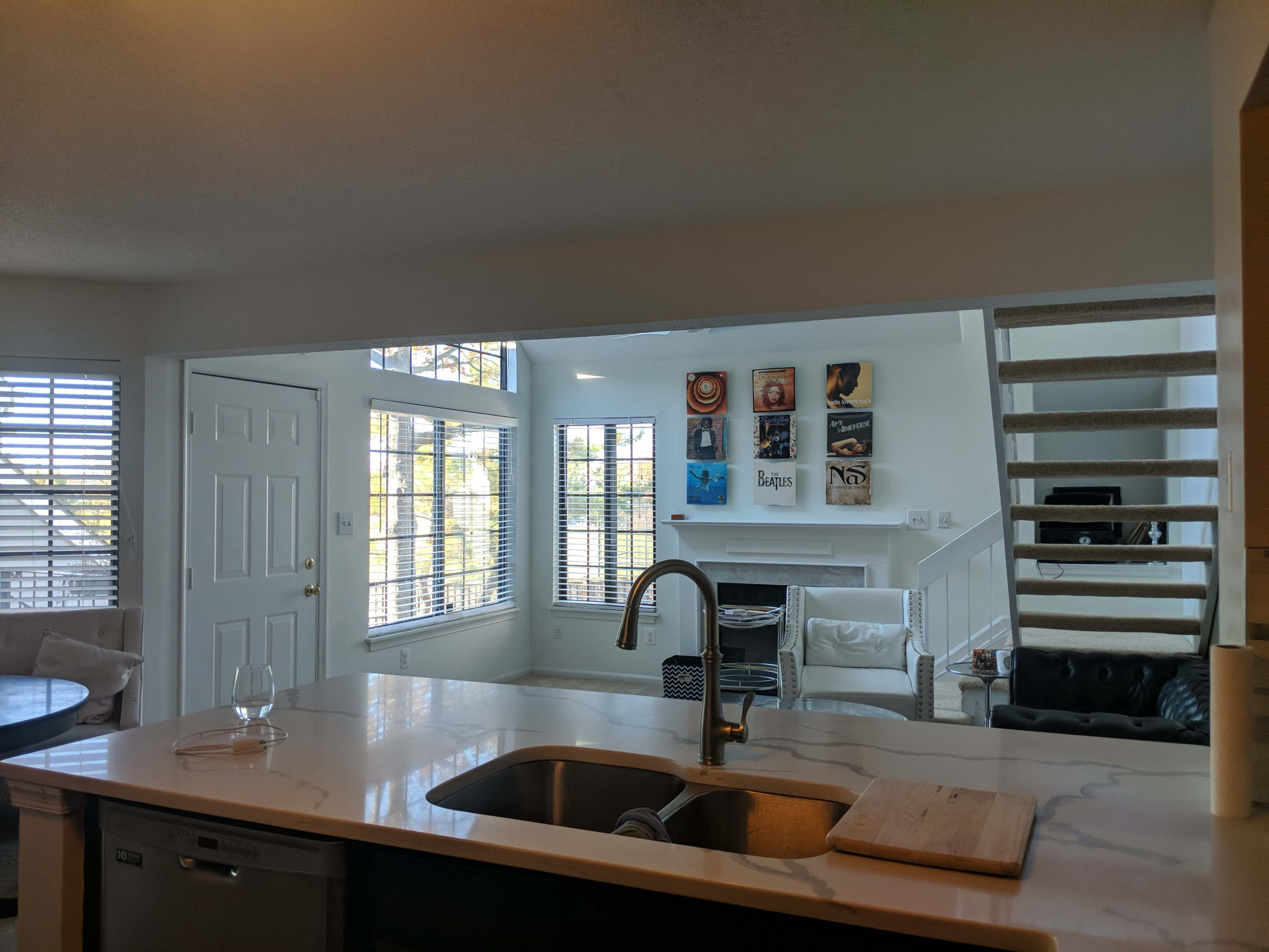 A bright, open-concept kitchen that leads into a living area featuring a staircase and artwork on the wall.