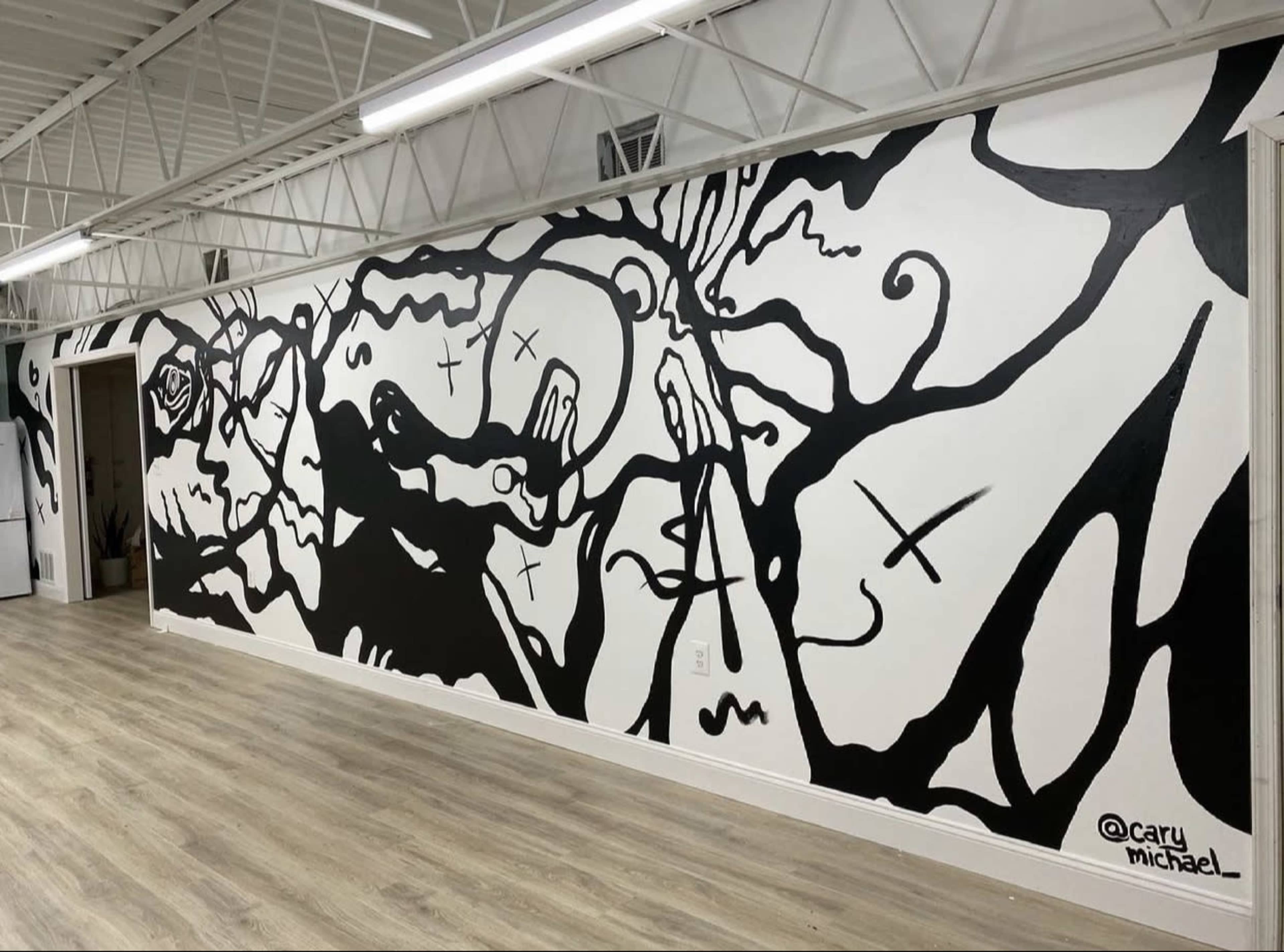 The image shows a black-and-white mural featuring abstract, intertwining shapes and figures on a wall within a spacious room.