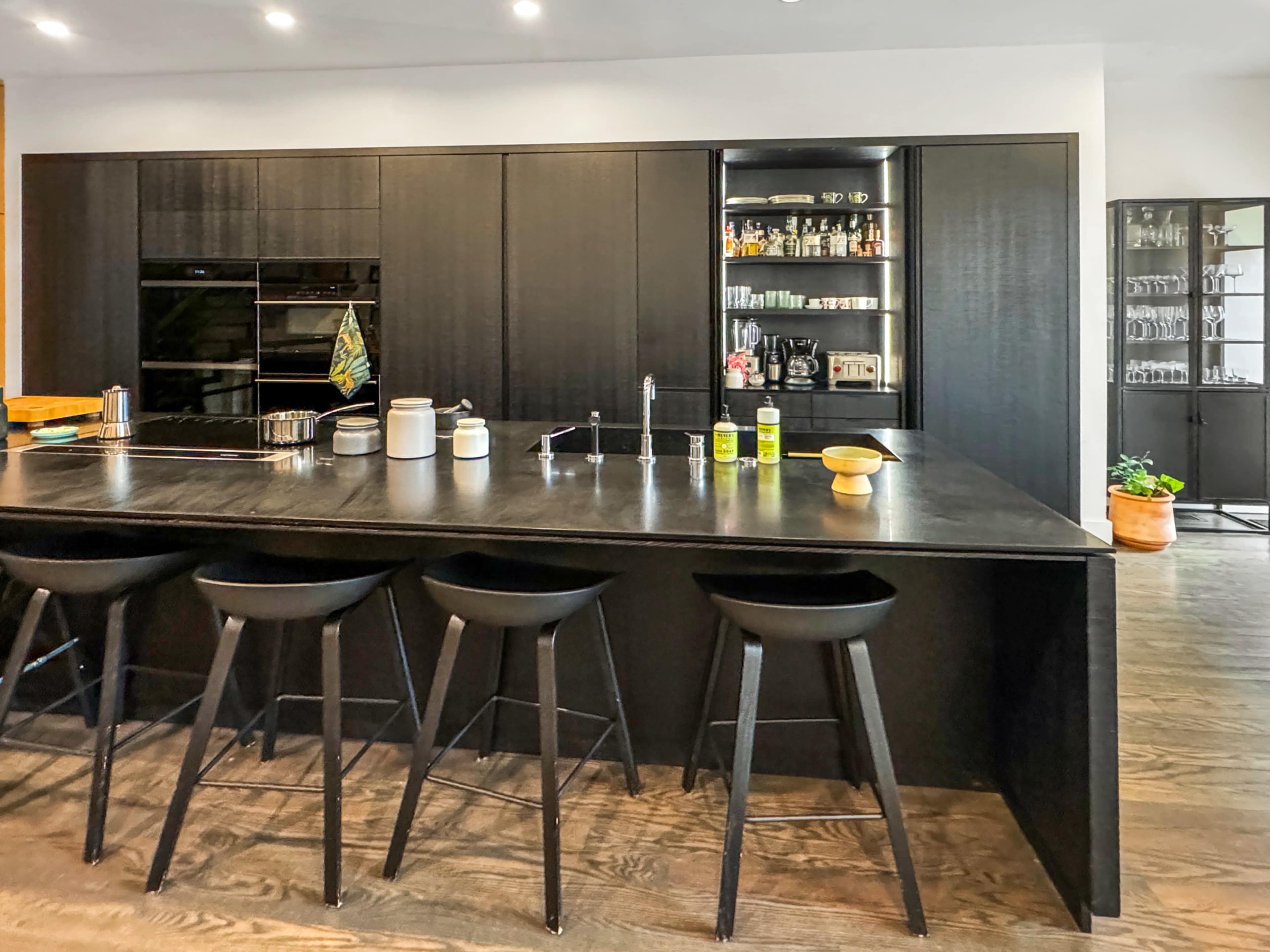 The image shows a modern kitchen with a large black island, sleek cabinetry, and high stools arranged around the island.