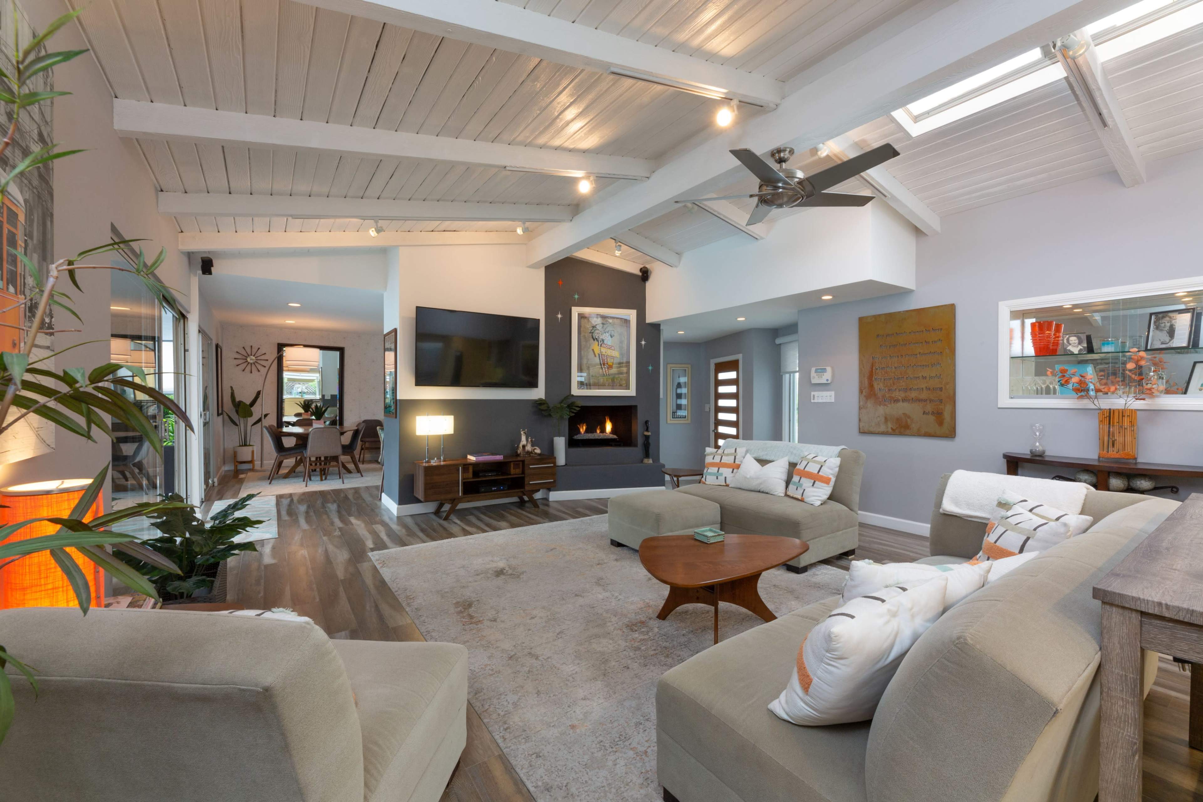 A modern living room with a high ceiling, featuring a seating area, a fireplace, a large flat-screen TV, and decorative artwork on the walls.