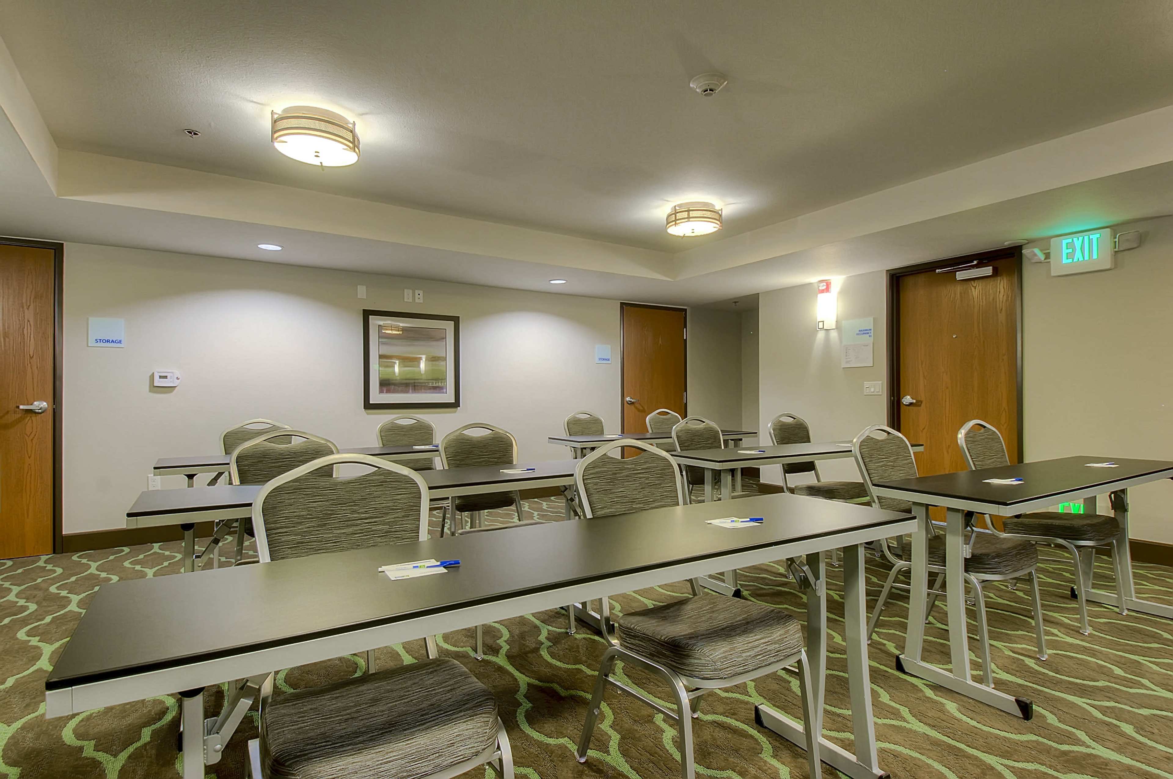 The image shows a simple meeting room with several rows of tables and chairs arranged for a presentation or workshop.