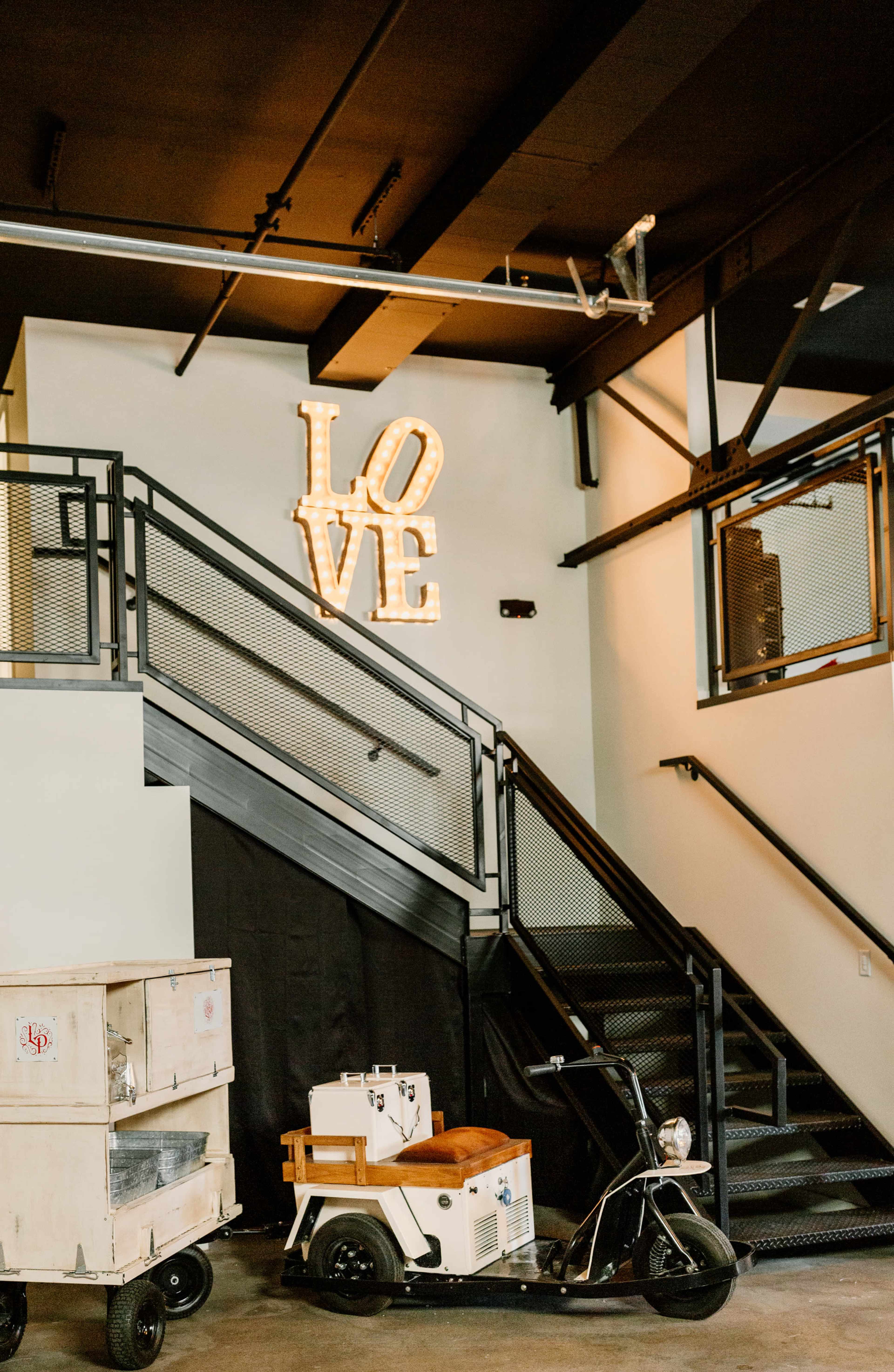 A staircase with a "LOVE" neon sign and a vintage scooter parked beside it.