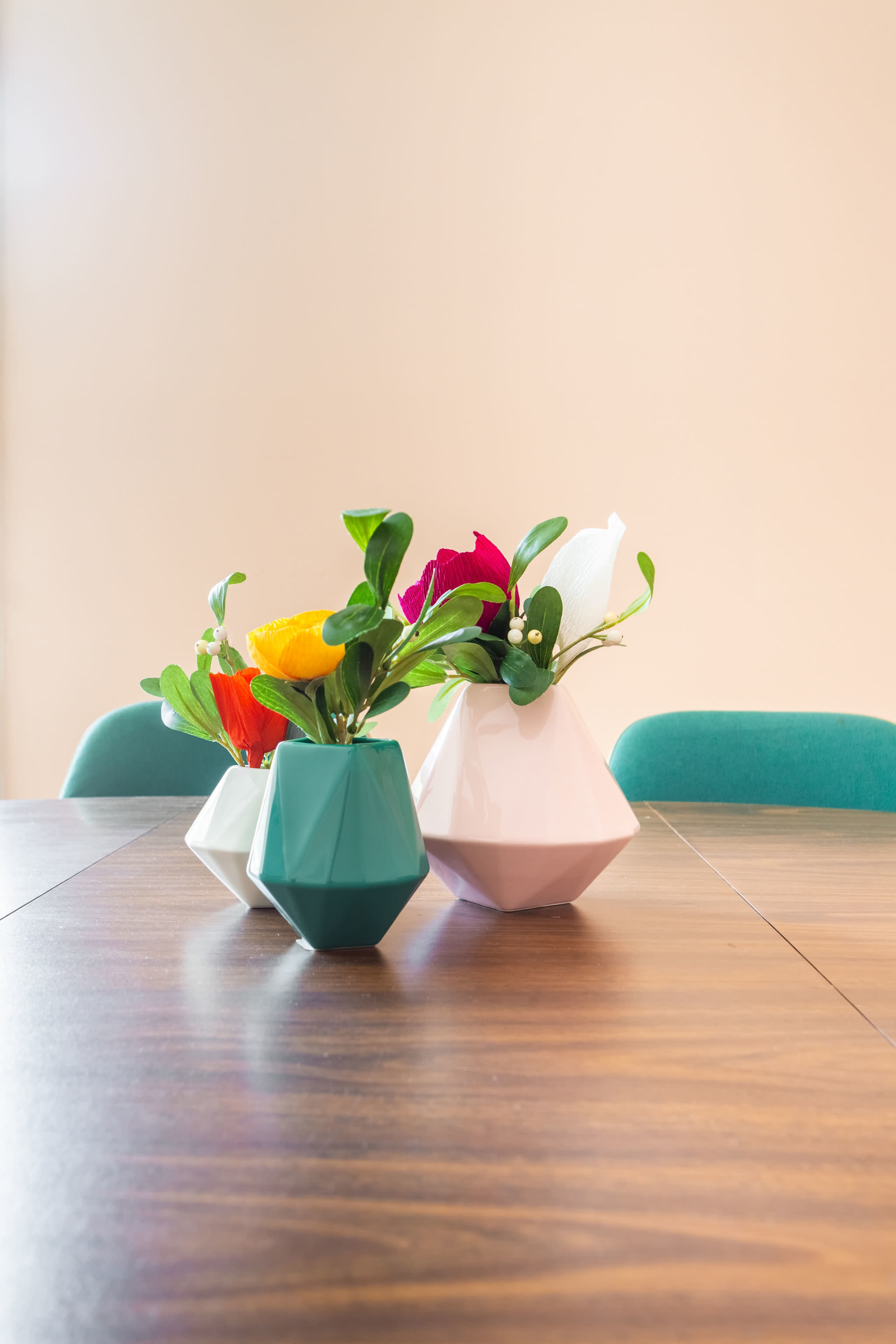 Three geometric vases with flowers are arranged on a wooden table.