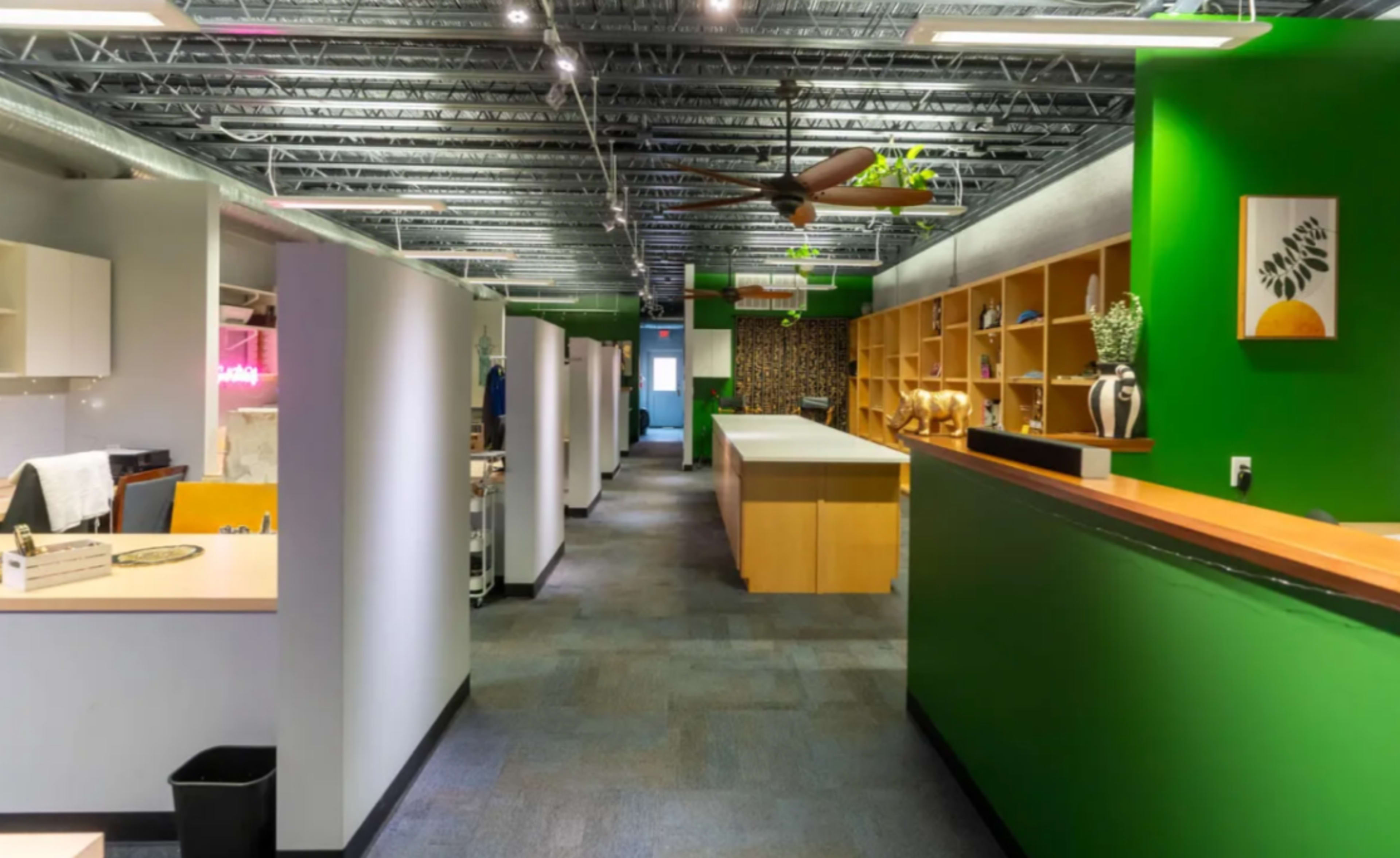A modern office space with green accent walls, several workstations, and a central reception area featuring shelving and decorative items.