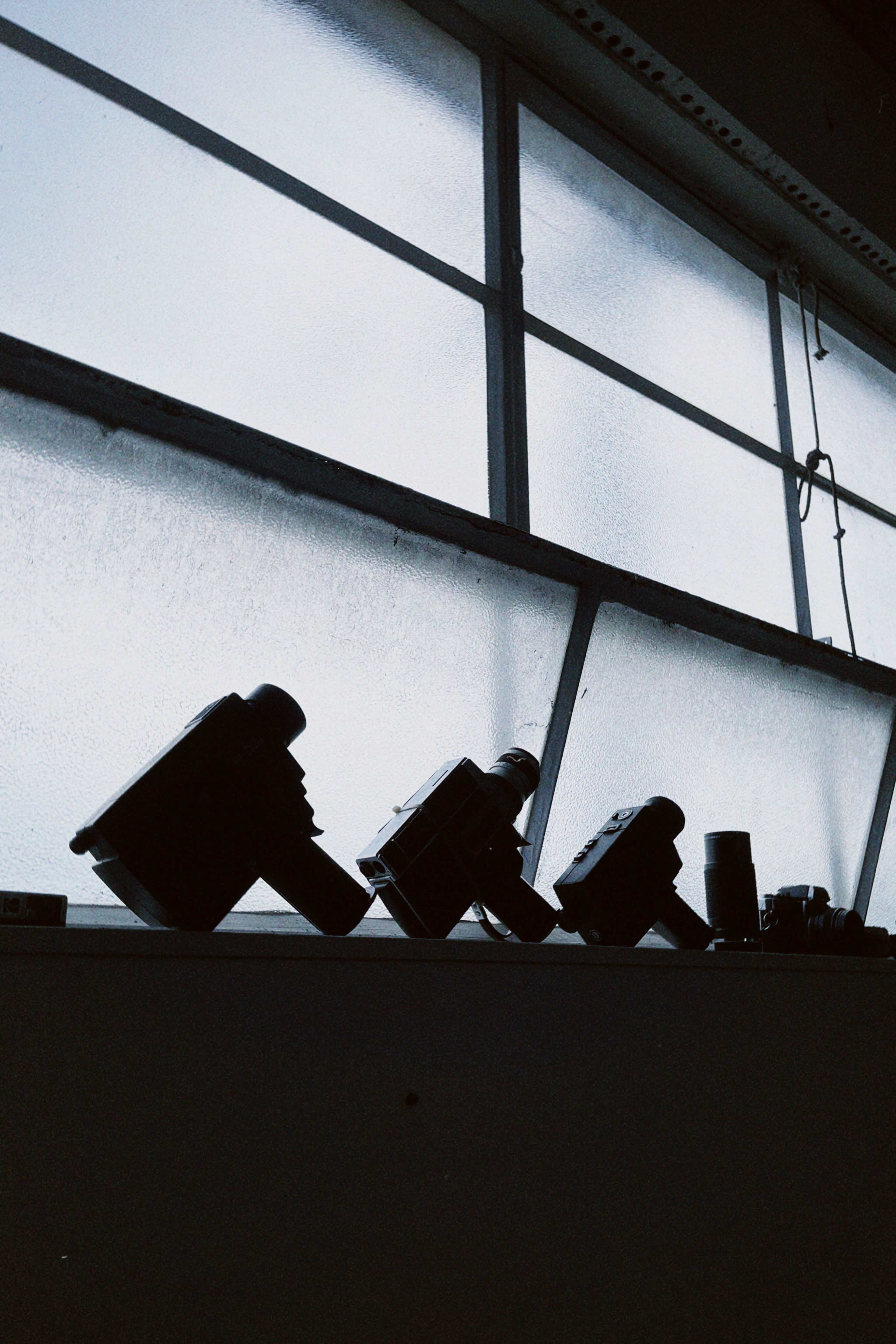 A row of cameras silhouetted against a window with frosted glass.