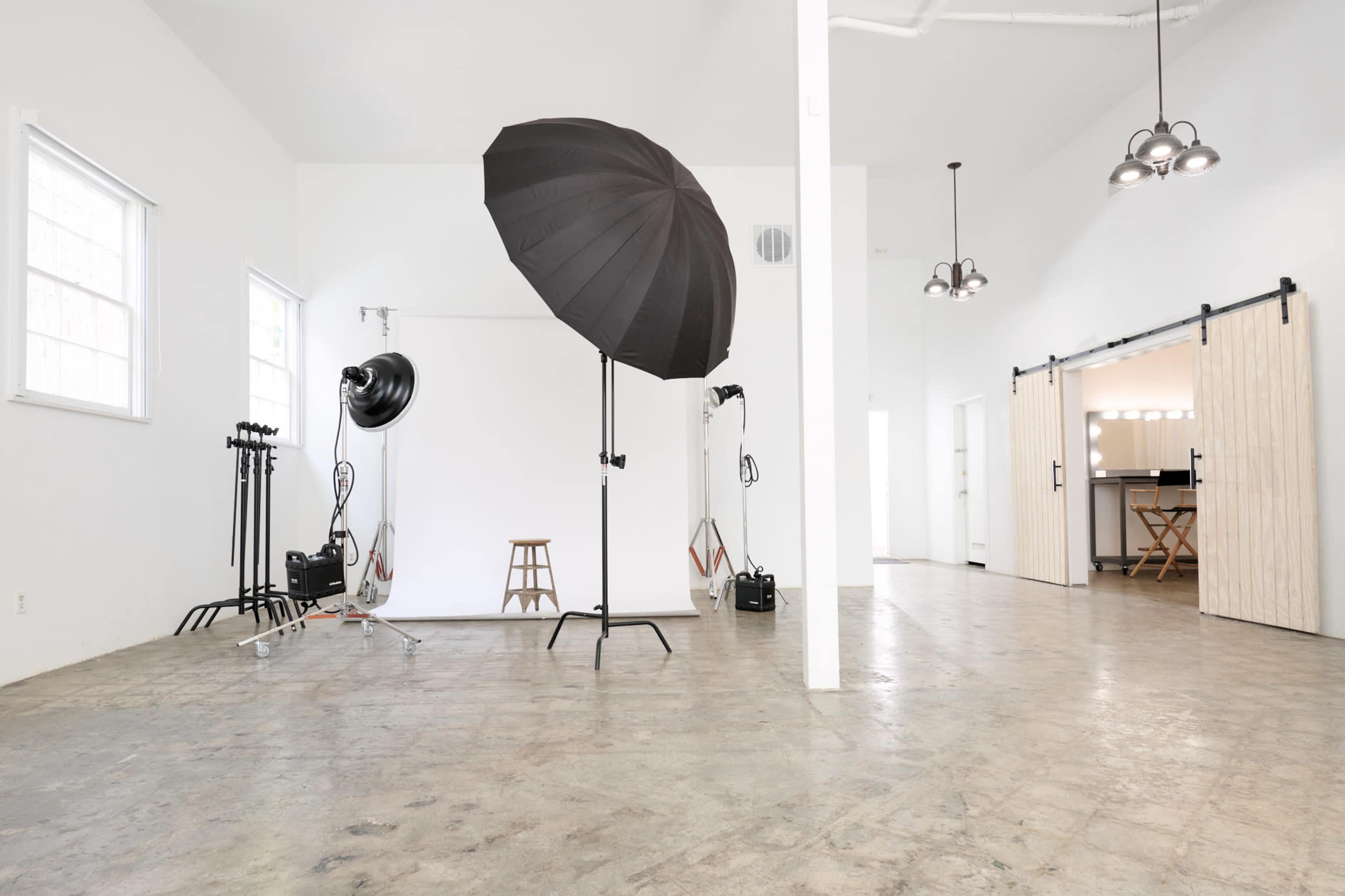 The image features a photography studio with a large black umbrella light, a backdrop, and various equipment on a polished concrete floor.