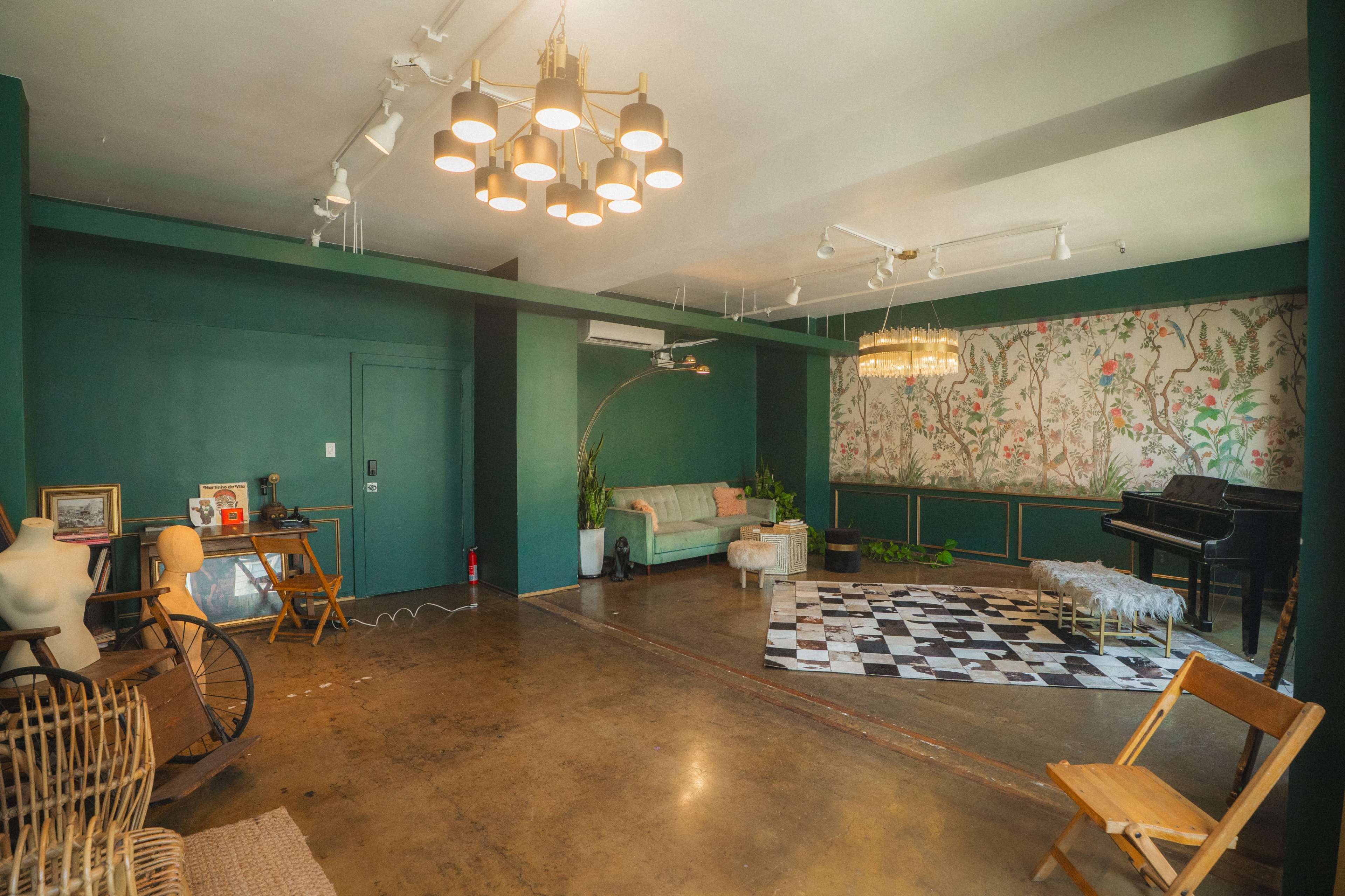 The room features a green color scheme with a couch, a piano, a patterned rug, and decorative plants.