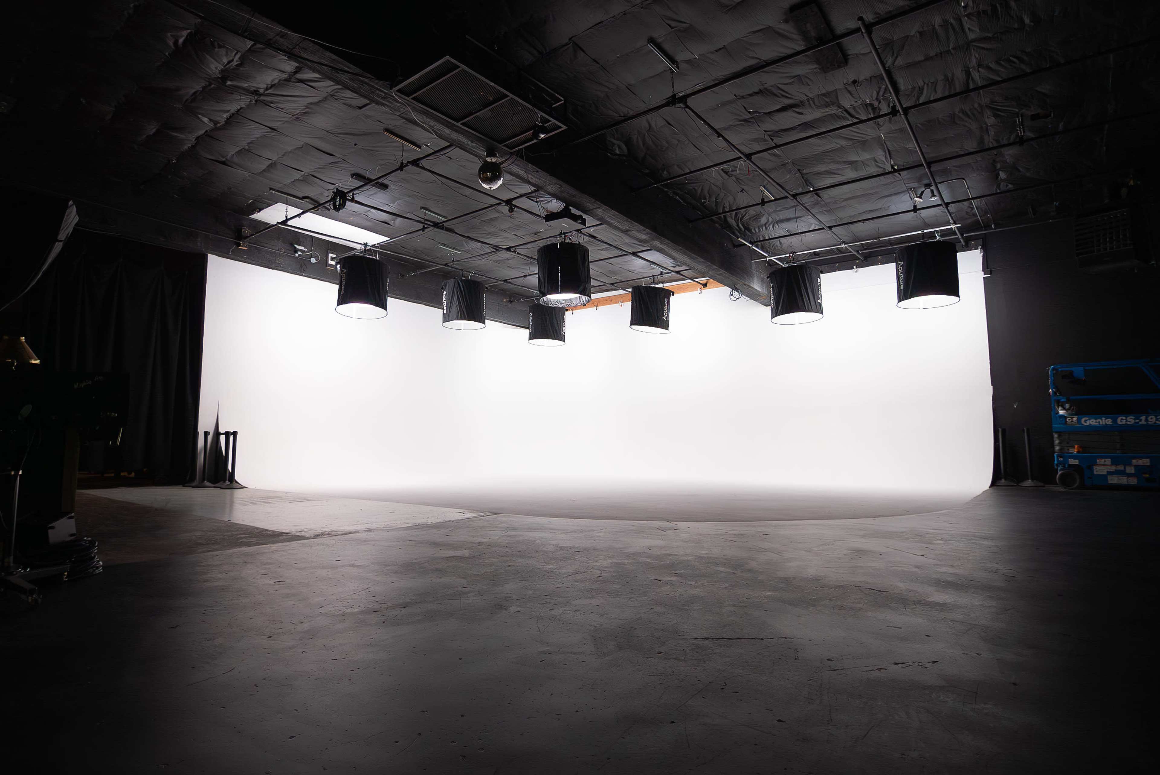 A large, empty photography studio features a smooth, white backdrop illuminated by multiple overhead lights.