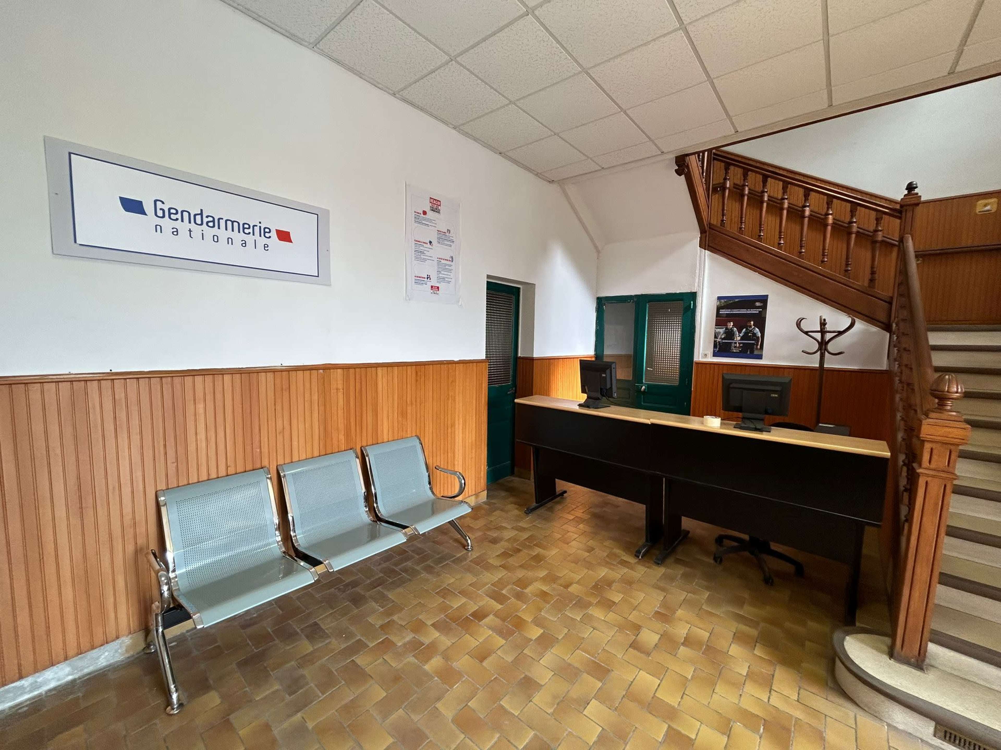The interior of a gendarmerie, featuring a reception desk, seating area, and a staircase.