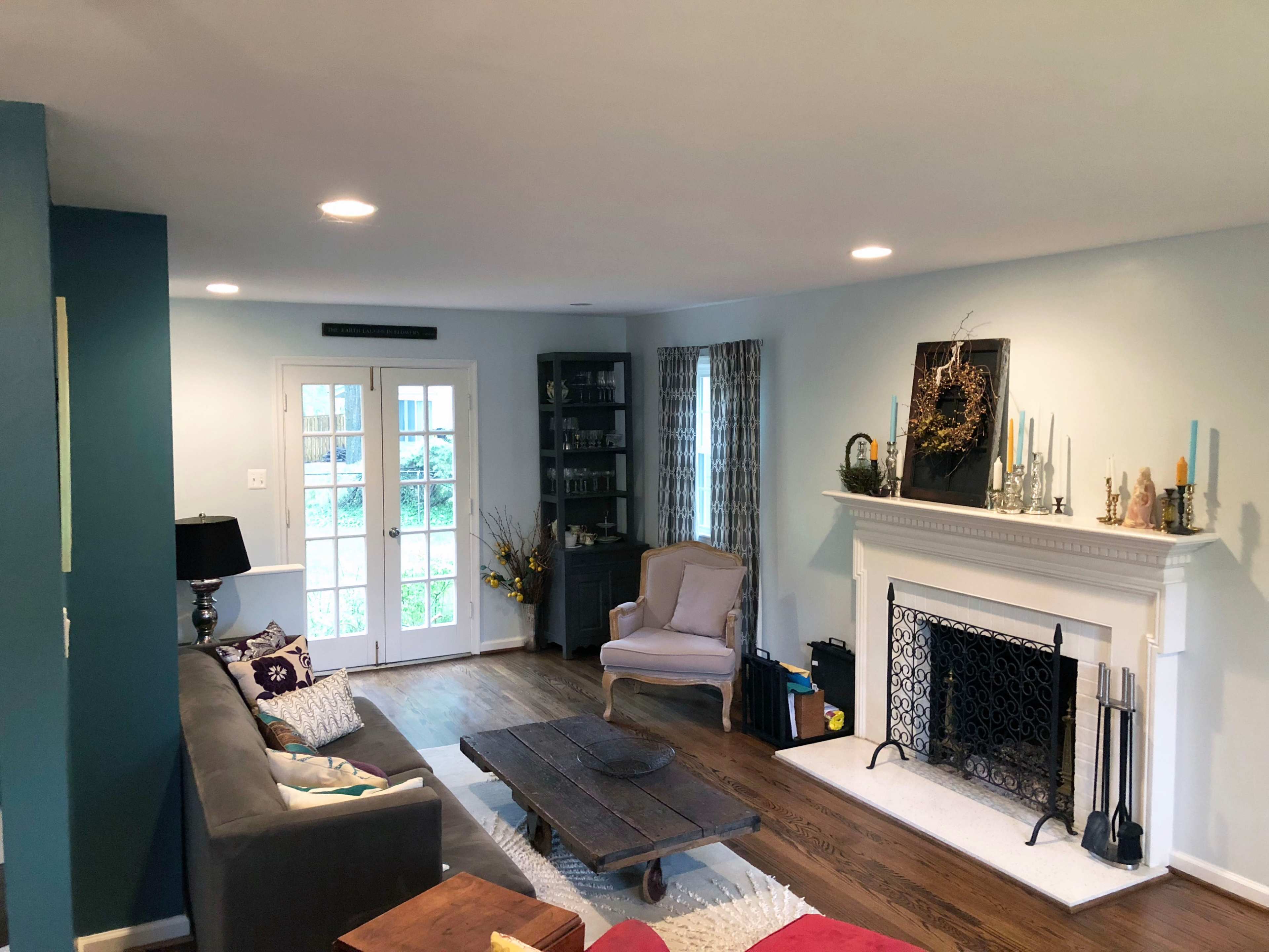A living room with a sofa, coffee table, armchair, fireplace, and large windows leading to an outdoor area.