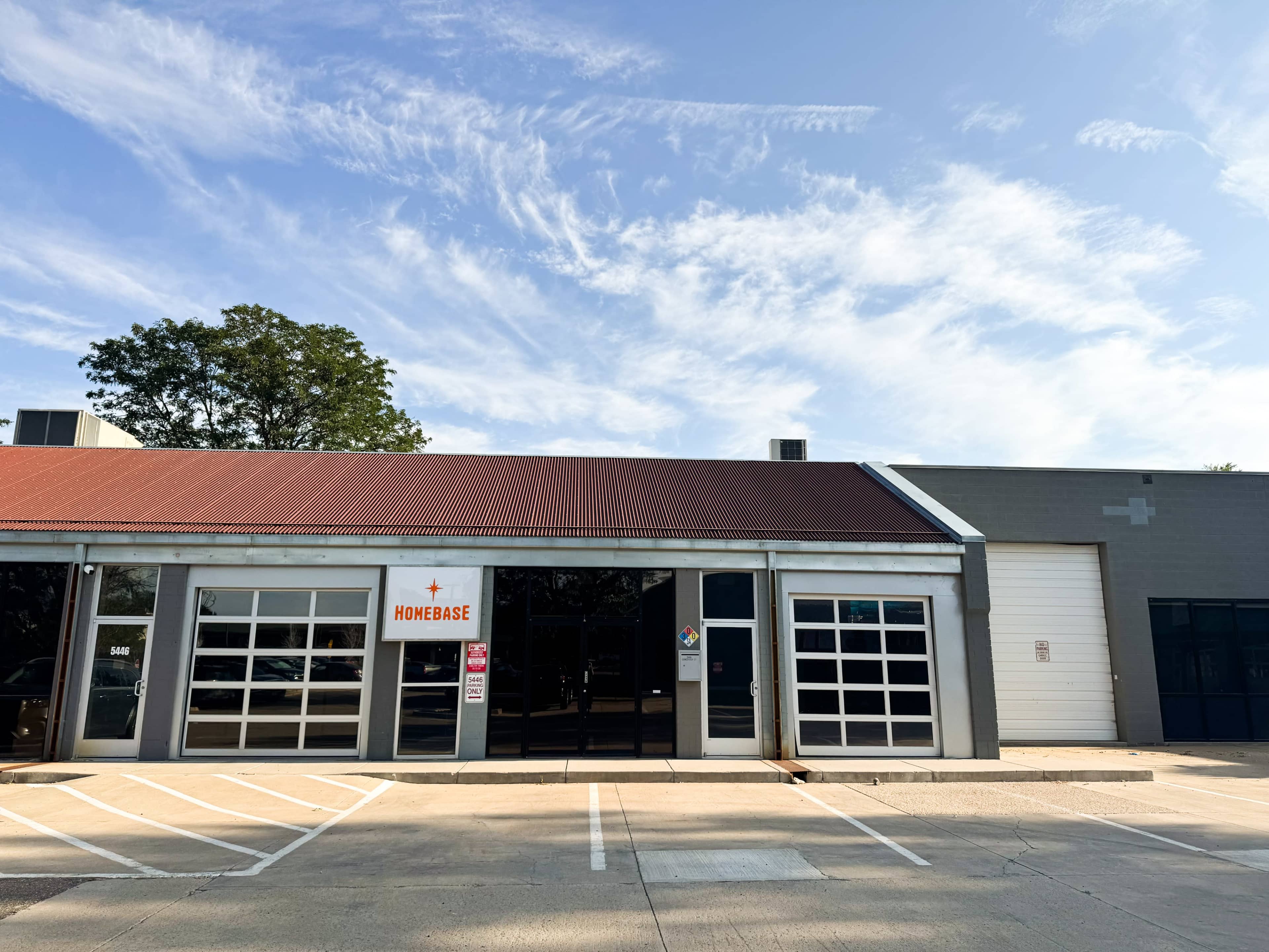 The image shows a commercial building with a red metal roof, large glass windows, and a sign reading "HOMEBASE."