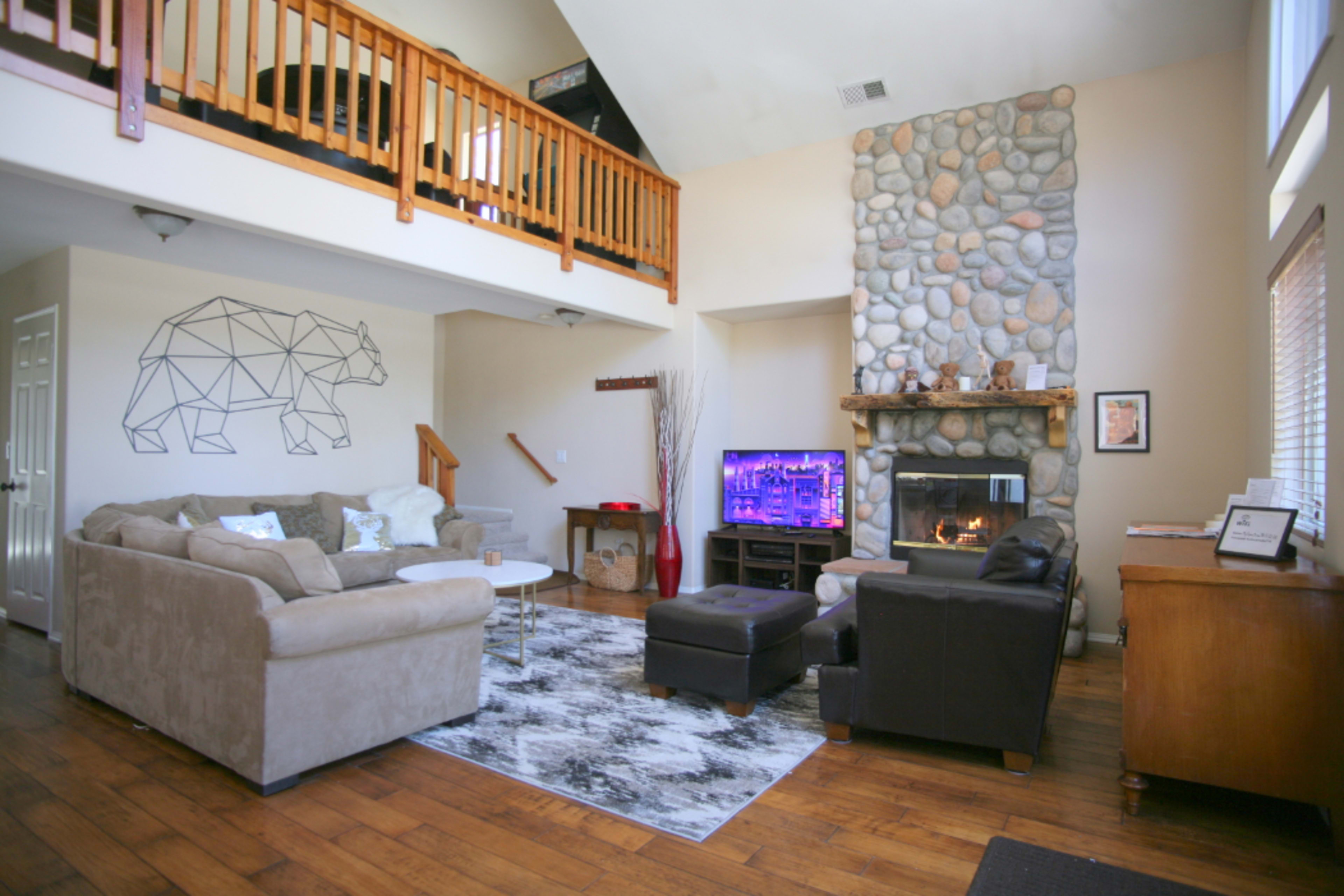 The living room features a stone fireplace, a mounted TV, a geometric bear design on the wall, and a mix of seating arrangements including sofas and a coffee table.