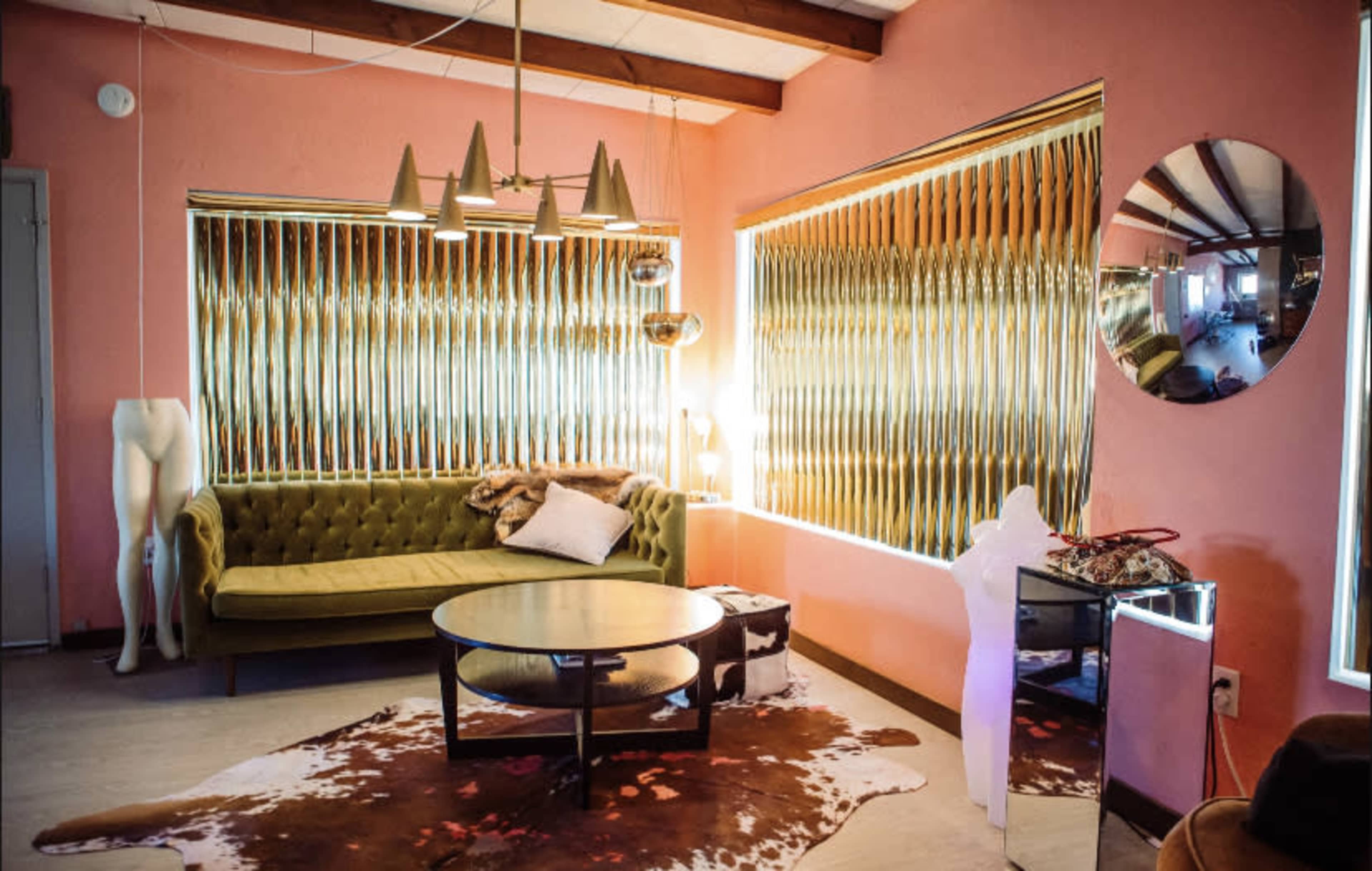 The image shows a modern interior with a green couch, a round coffee table, and large windows adorned with golden vertical blinds.