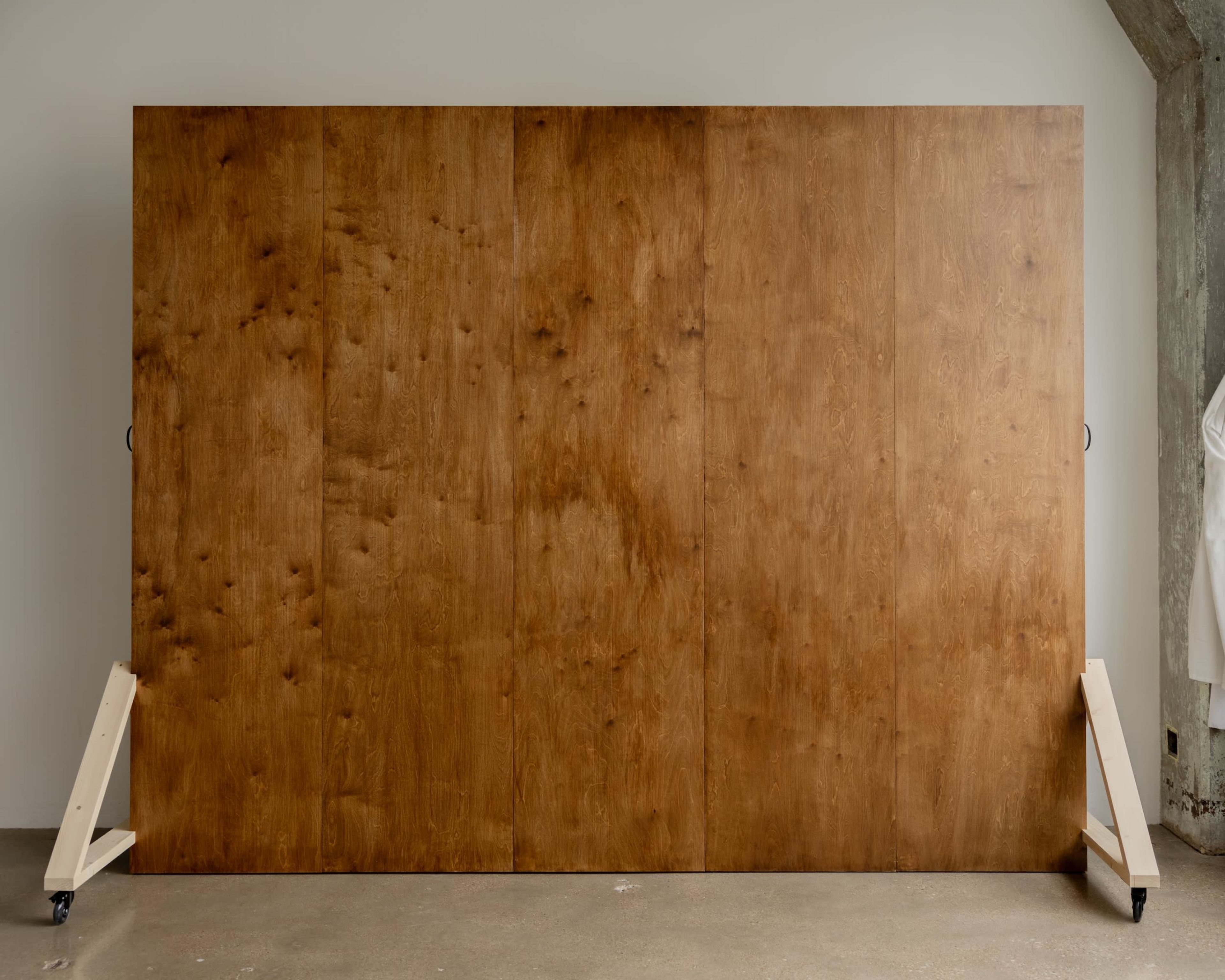 A large wooden panel with a smooth, warm finish stands on two wooden supports in an indoor space.