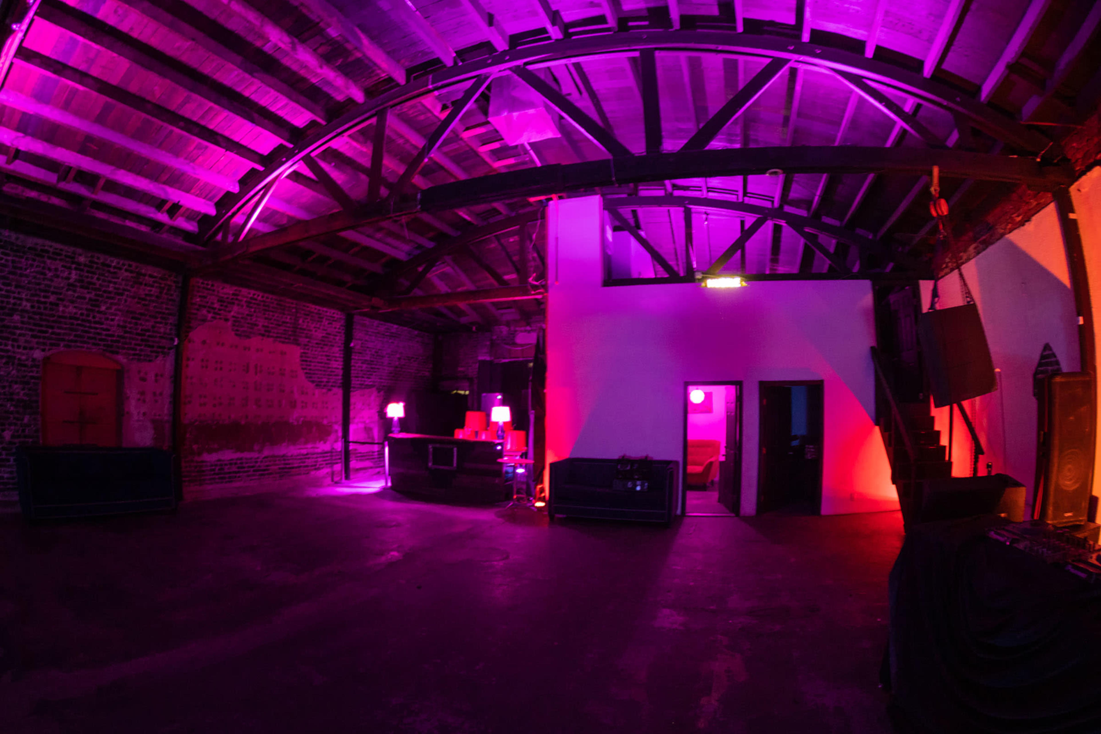 A large, industrial space features exposed brick walls, a wooden ceiling, and vibrant purple lighting throughout.