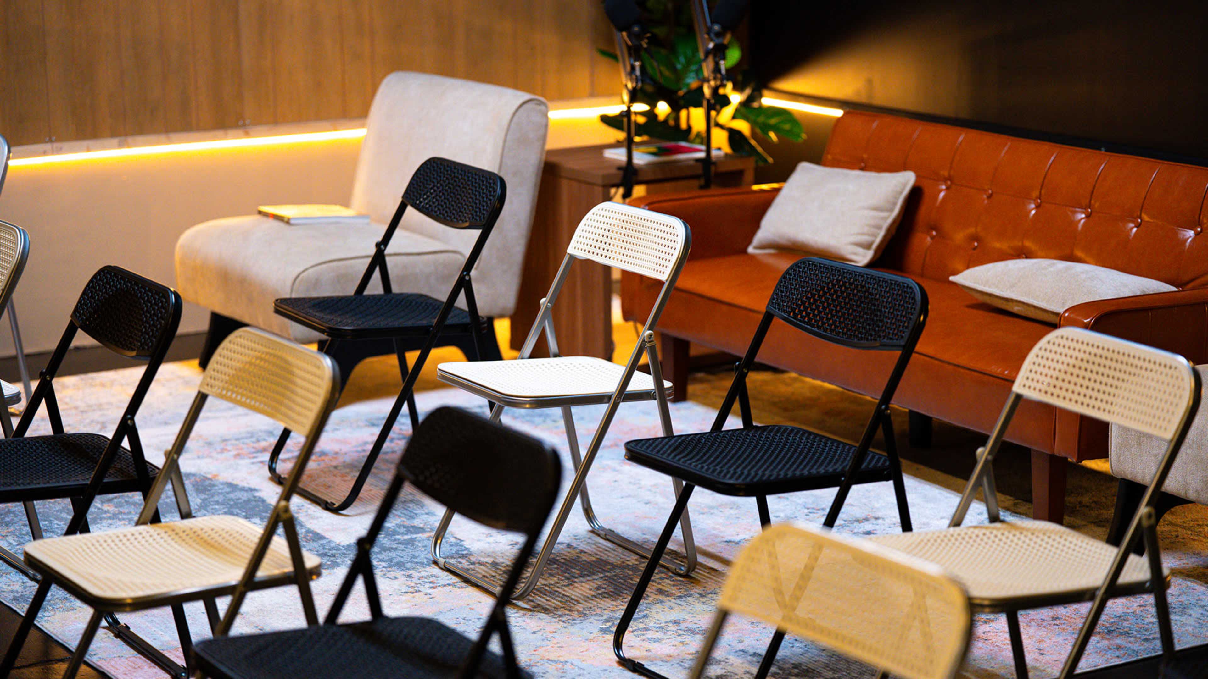 The image shows a small seating area featuring various styles of chairs, including folding chairs and an upholstered sofa, arranged on a patterned rug.