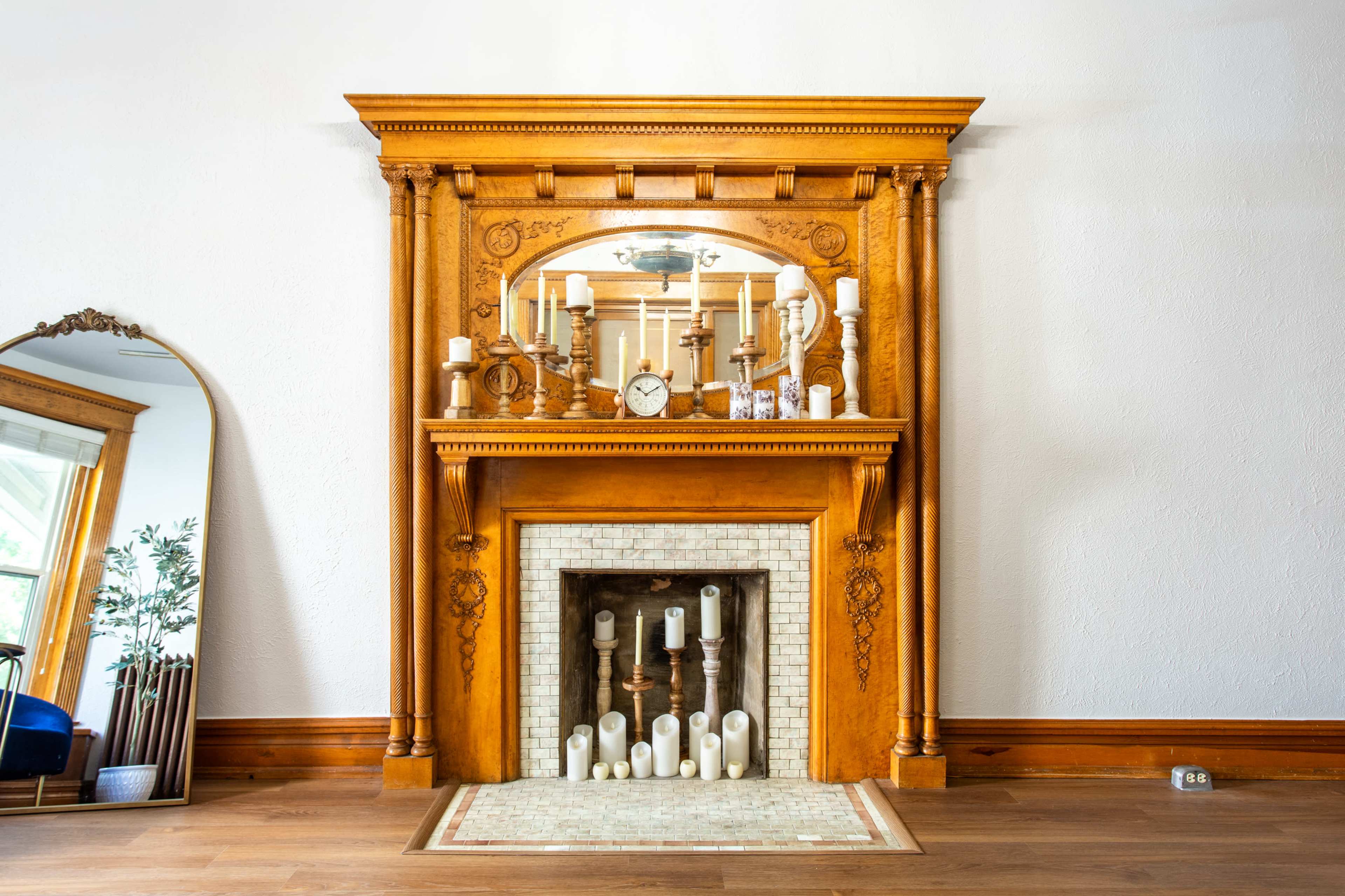 A wooden fireplace mantel adorned with various candles and decorative items, set against a plain white wall.