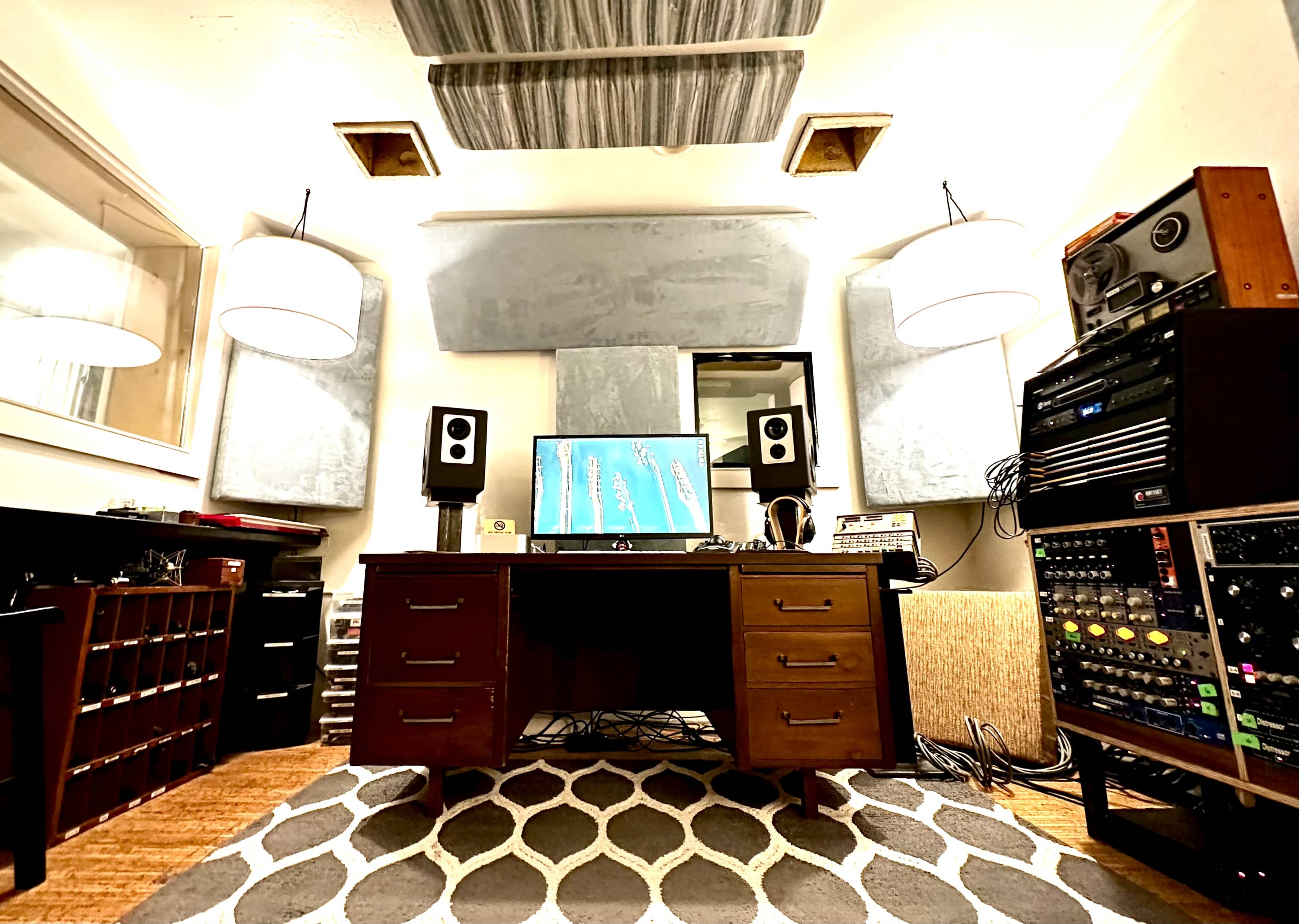 A music studio with a central desk, audio equipment racks, and soundproofing panels on the walls.