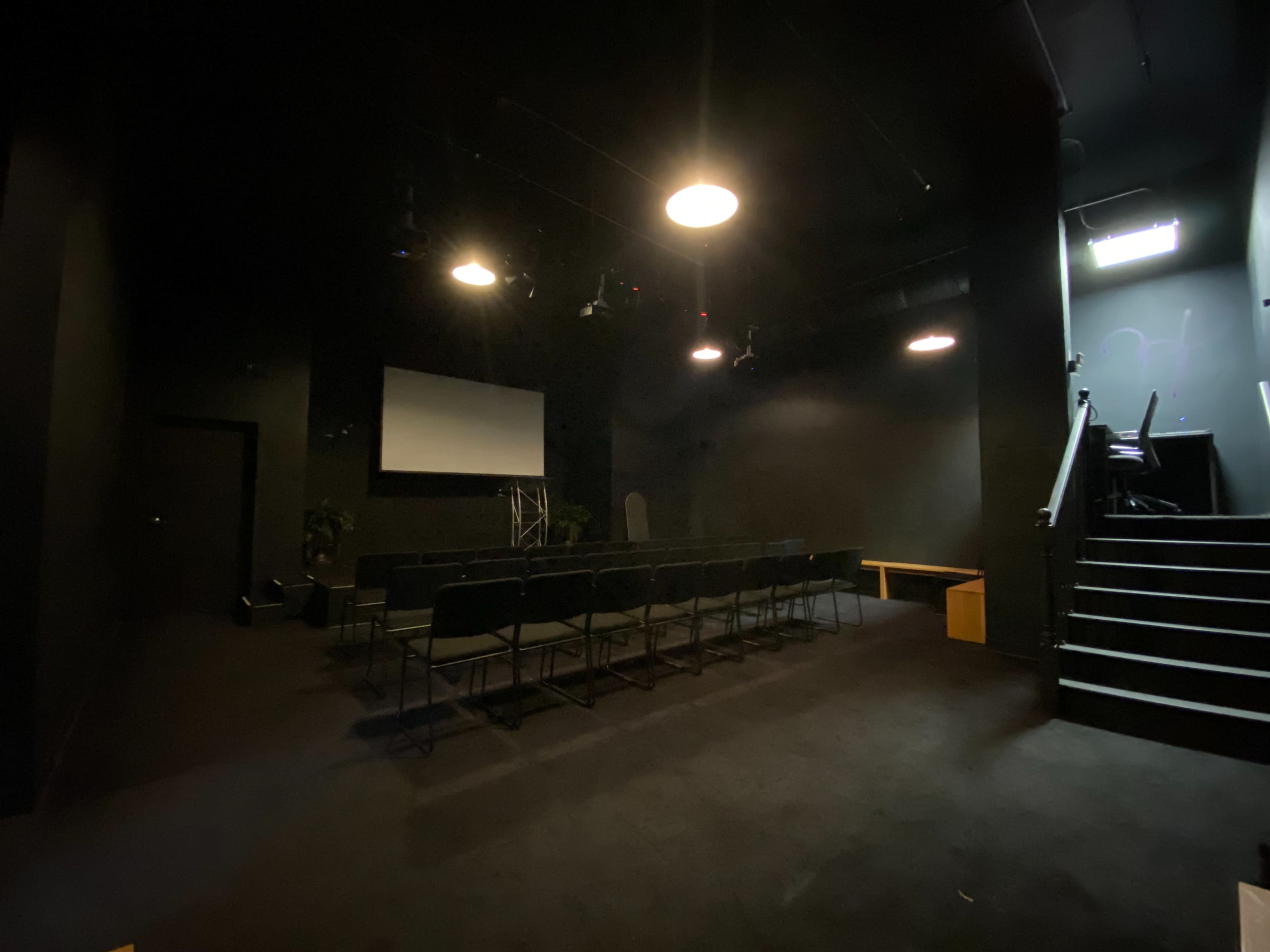 A dark room with a seating area, a screen at the front, and a staircase leading to an upper level.