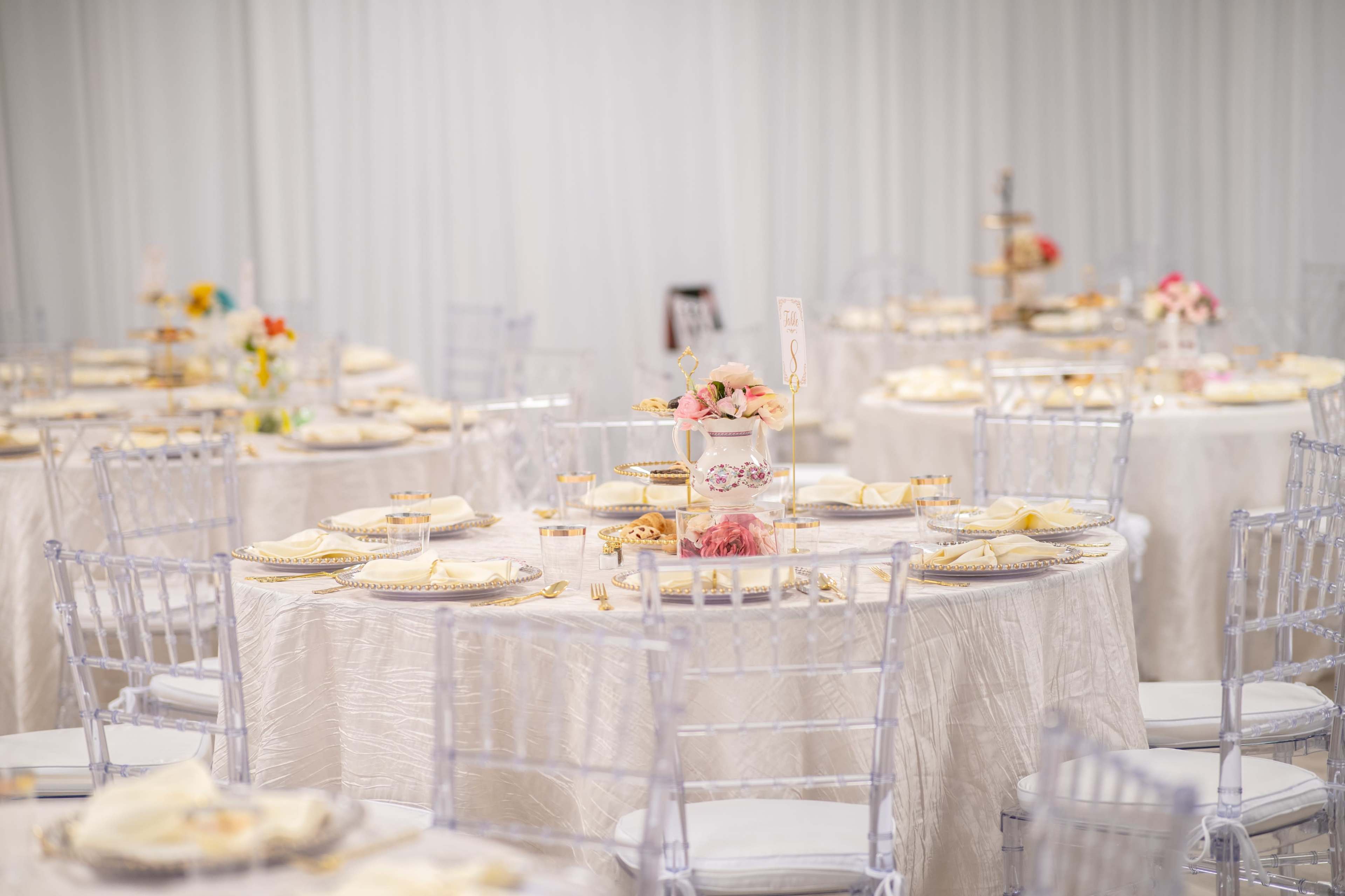 The image features elegantly set tables with white tablecloths, adorned with floral centerpieces and fine china, arranged in a well-lit banquet hall.