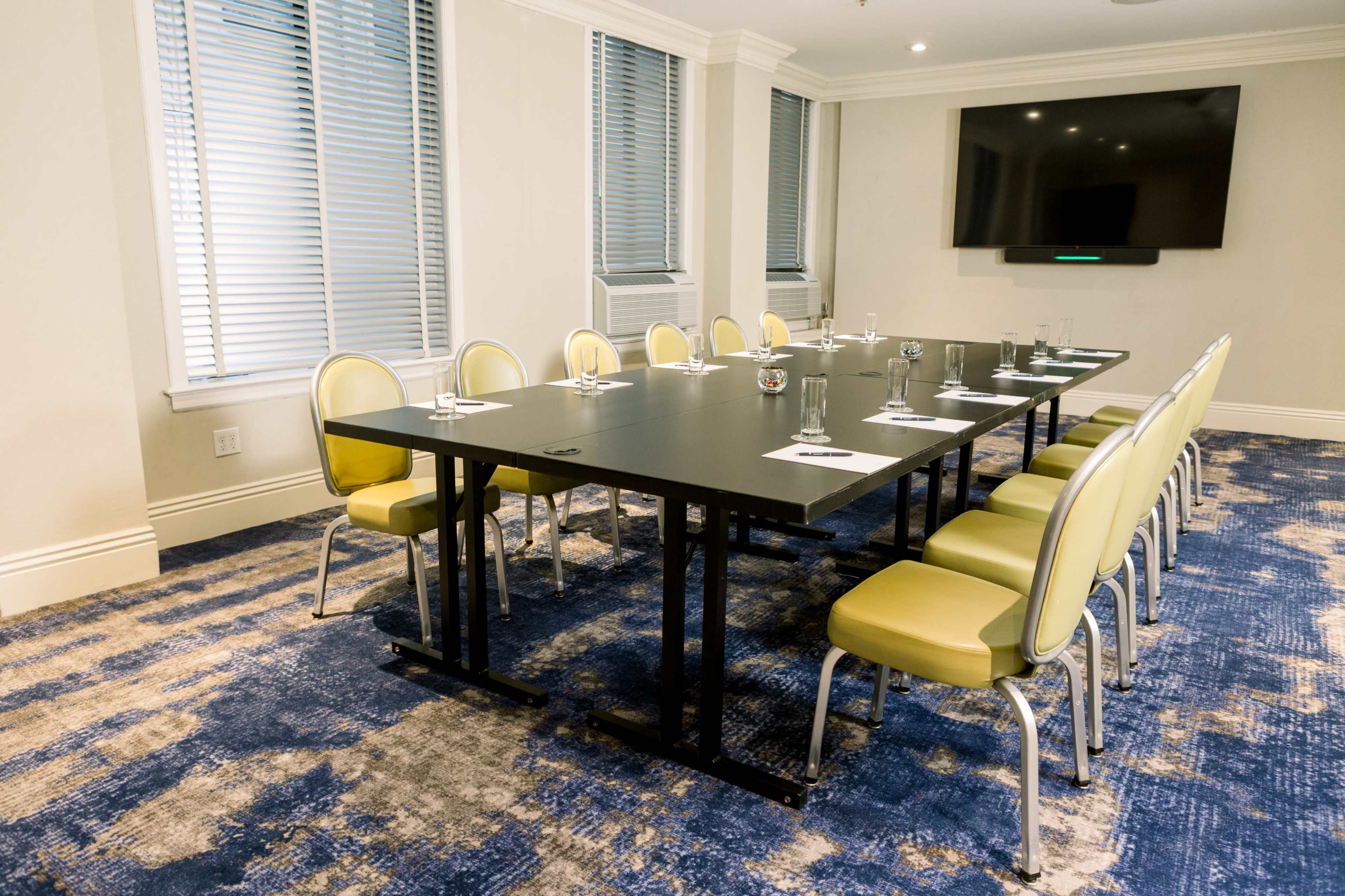 A long conference table is set with glasses and notepads, surrounded by yellow chairs in a well-lit meeting room.