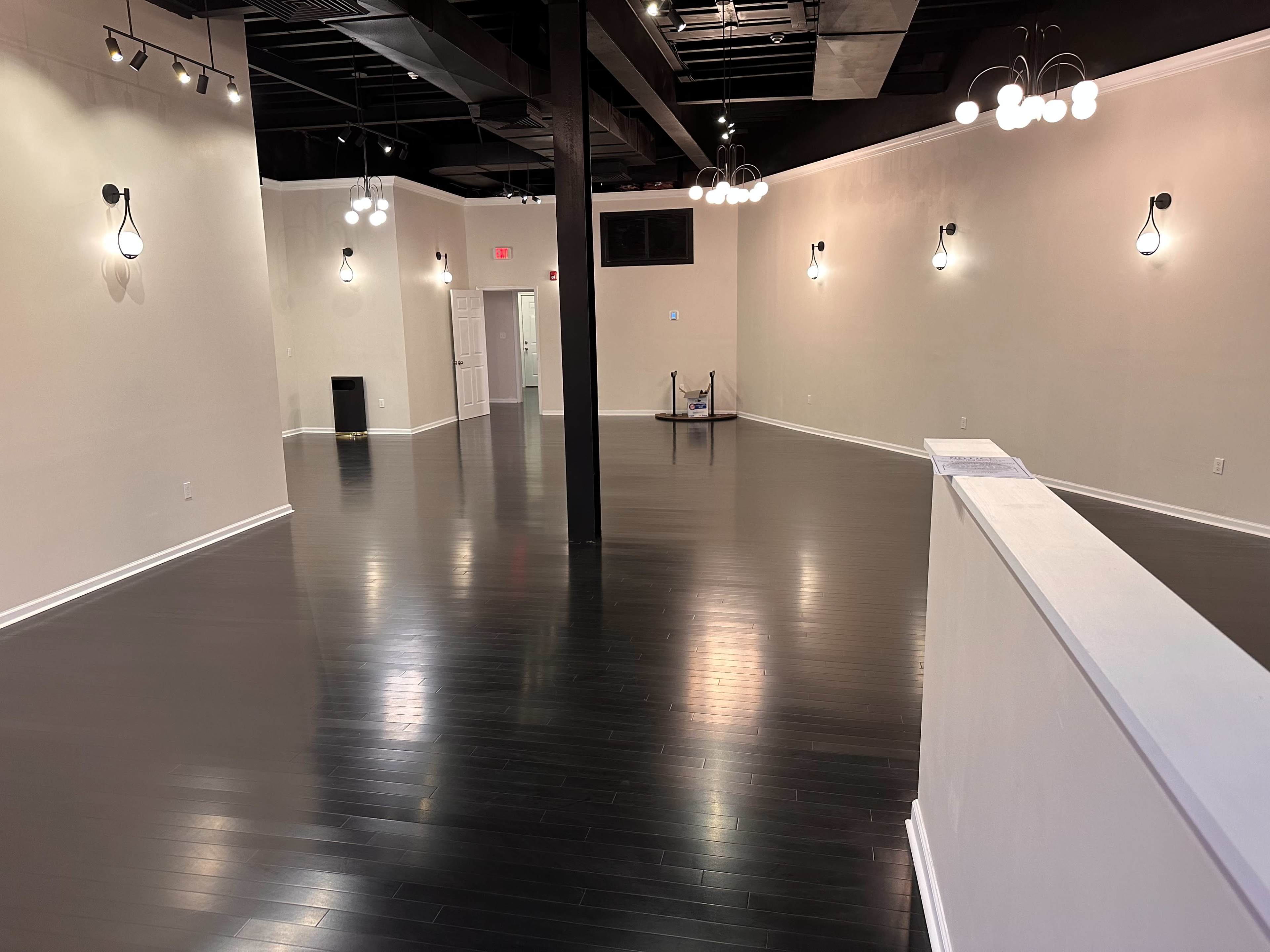 The image shows a spacious, empty room with black wooden flooring and several light fixtures mounted on the walls.