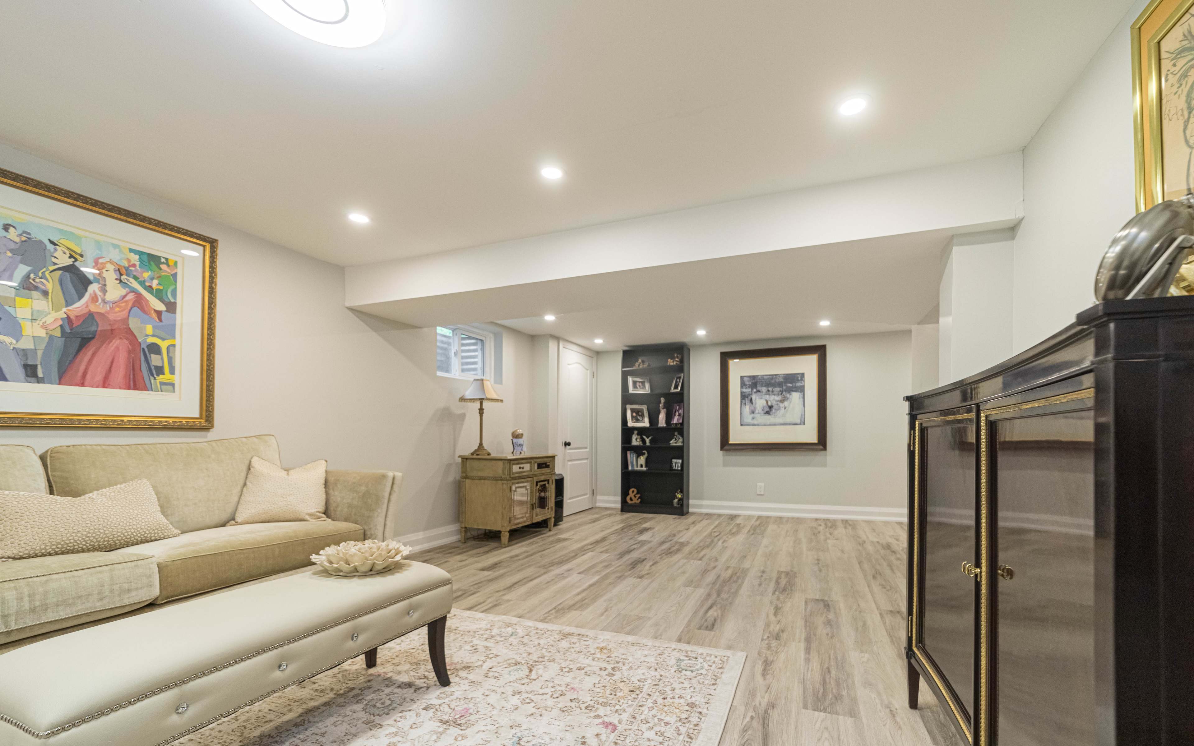 A modern, well-lit basement living space featuring a light-colored sofa, a decorative rug, and a gallery wall with framed artworks.
