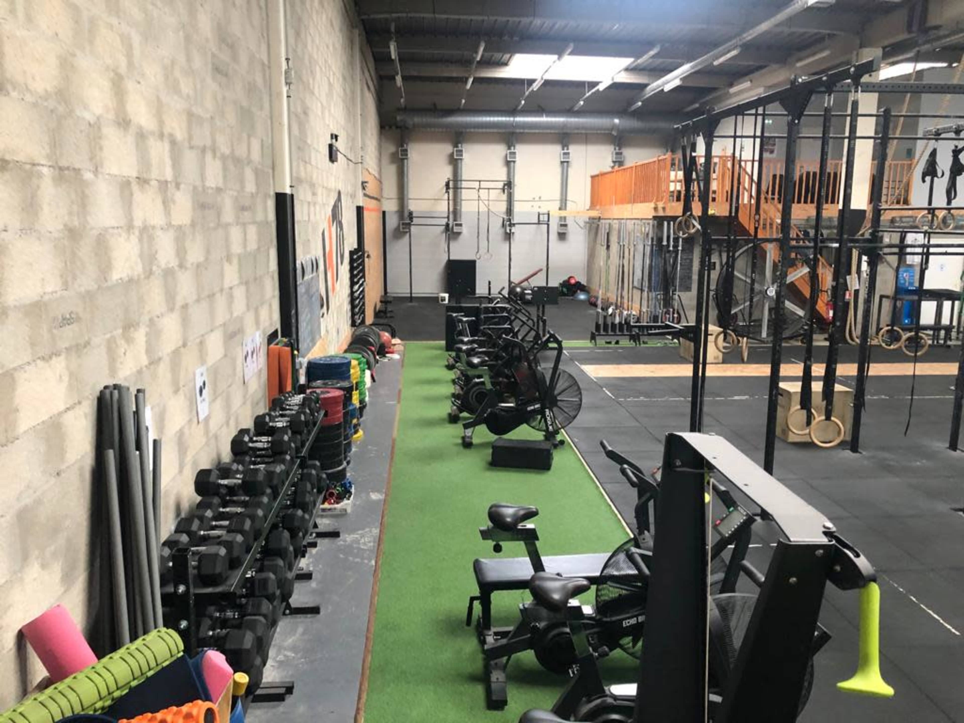 An indoor gym with workout equipment, including weights, exercise bikes, and a climbing frame, set against a textured gray wall.