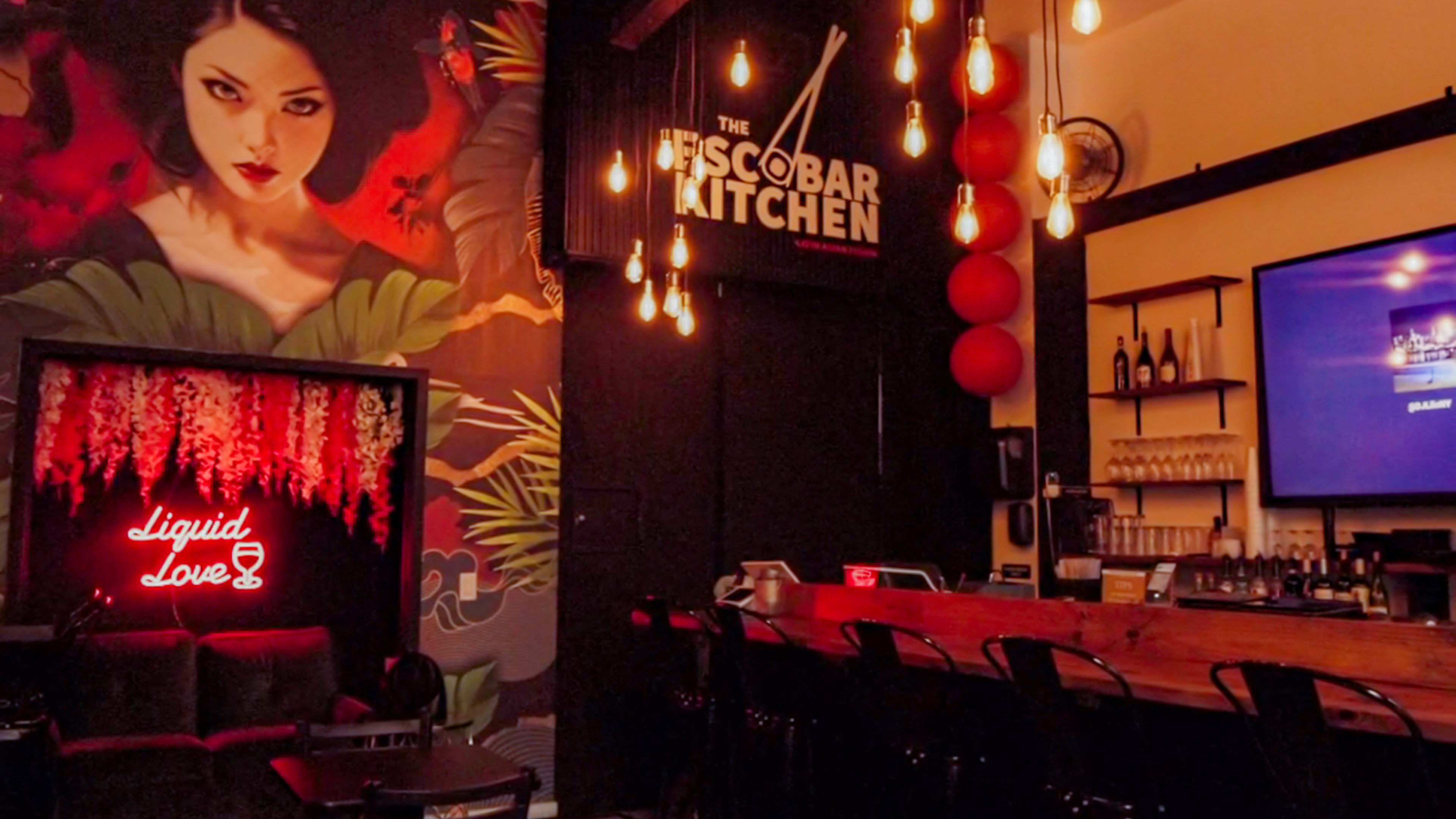 The image features a dimly lit bar area adorned with a vibrant mural, pendant lights, and a neon sign that reads "liquid Love."