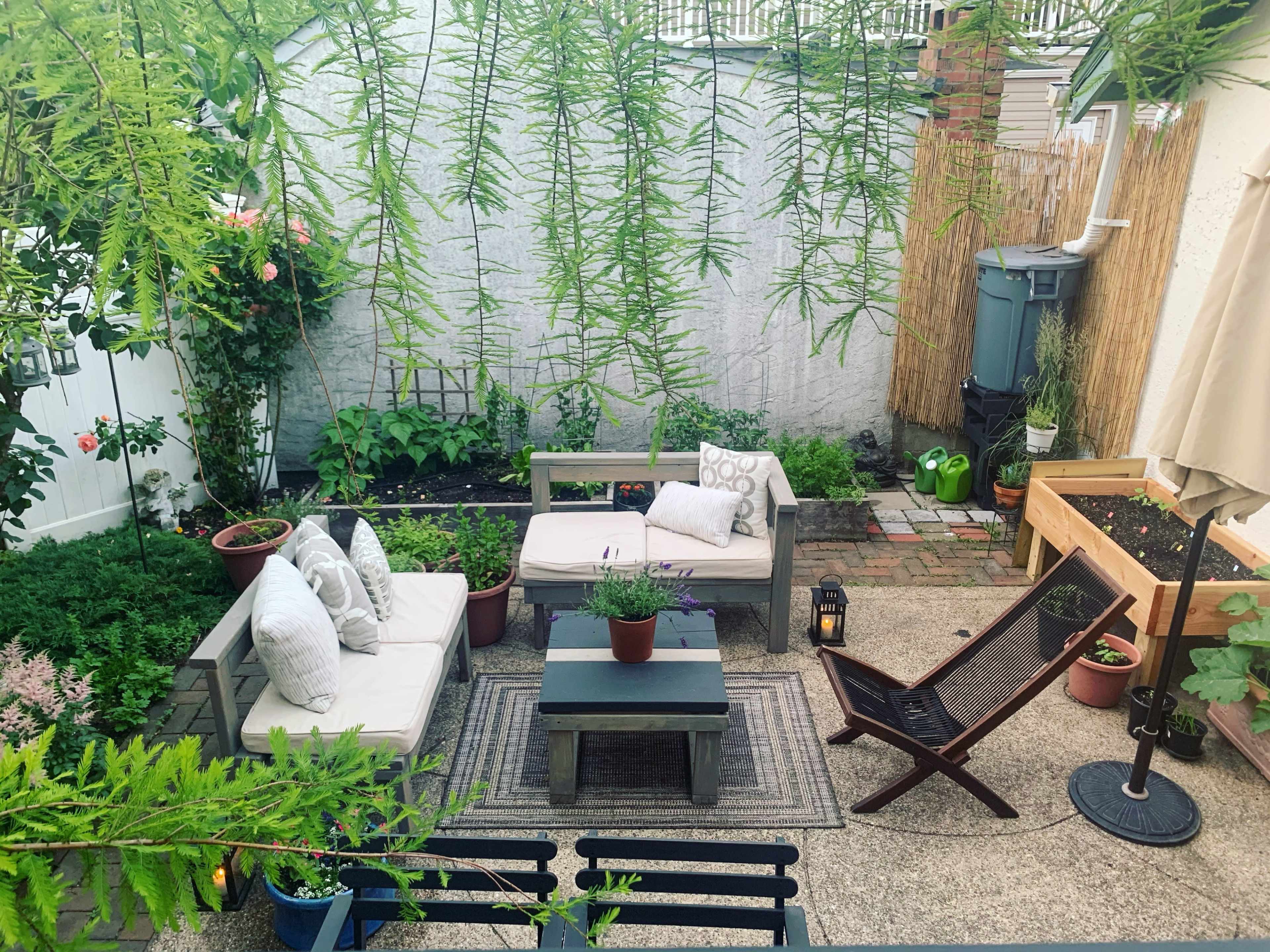A small, well-maintained garden patio with seating arrangements, potted plants, and a barbecue area.