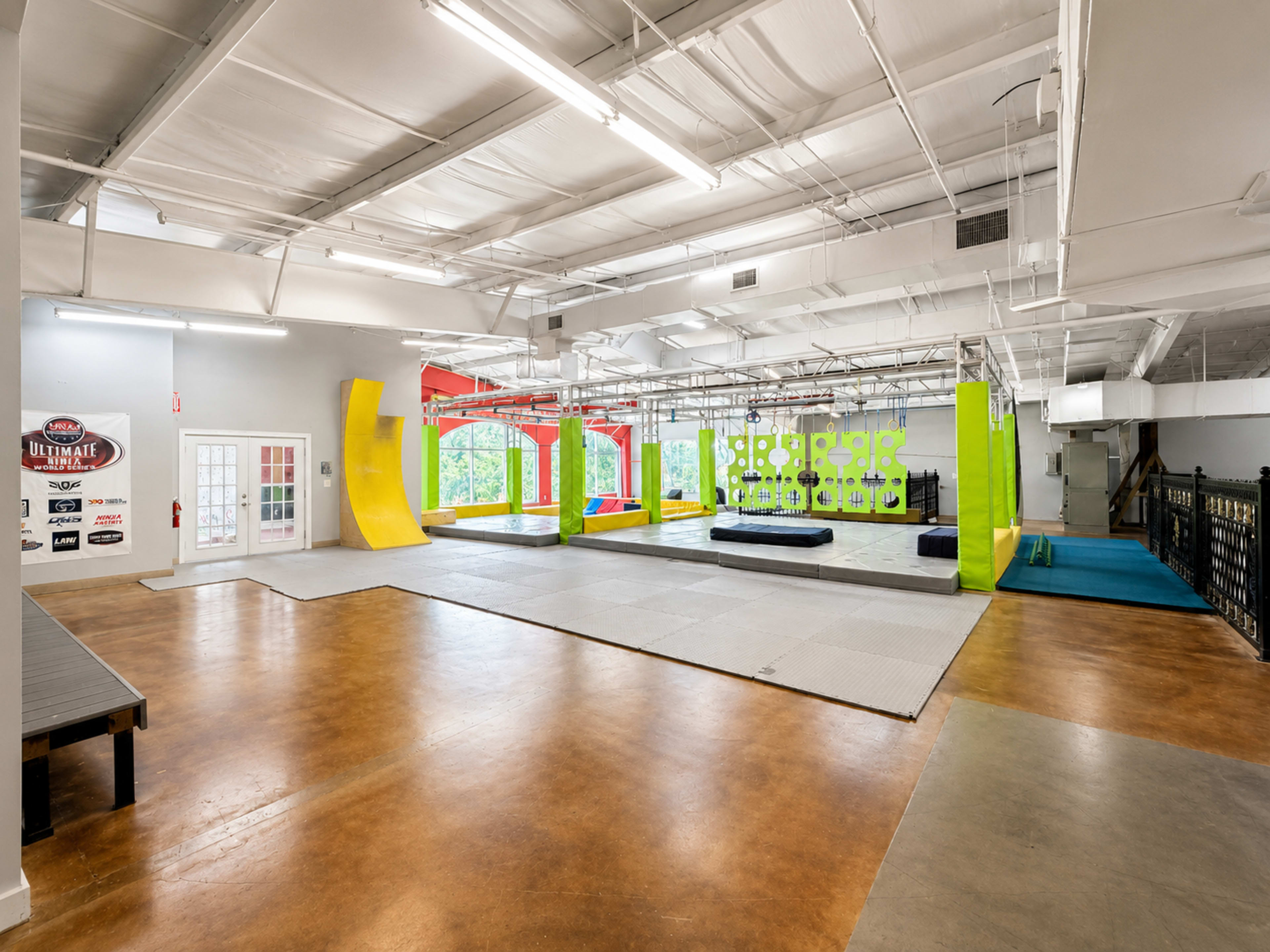 The image shows a spacious indoor gym designed for activities, featuring various colorful climbing walls, mats, and open areas for exercise.