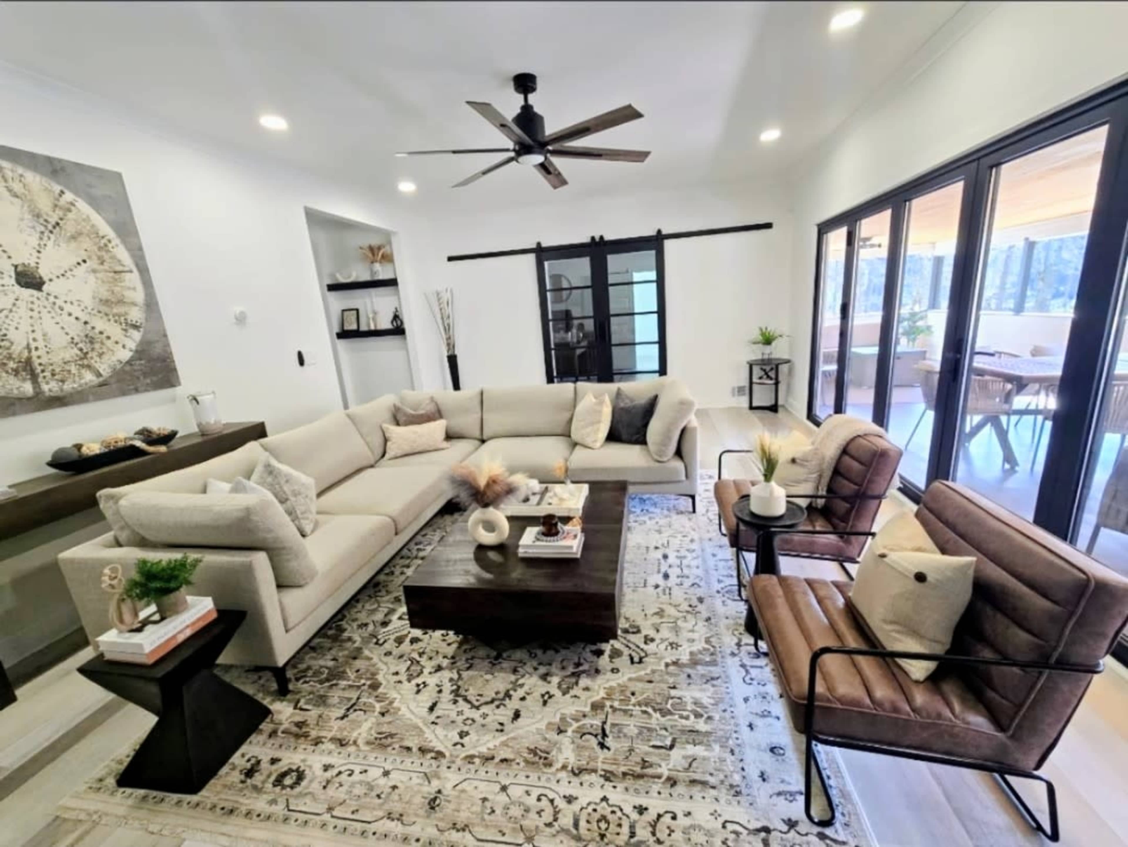 The image shows a modern living room with a large sectional sofa, two accent chairs, a coffee table, and a decorative area rug.