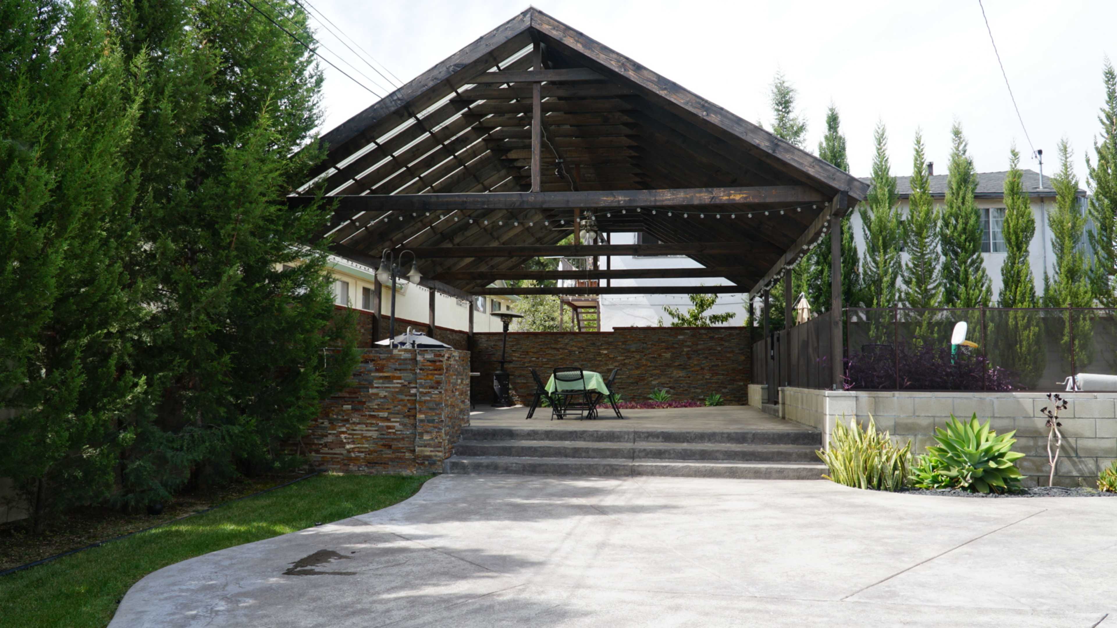 A covered outdoor patio features stone walls, a seating area, and landscaped greenery.